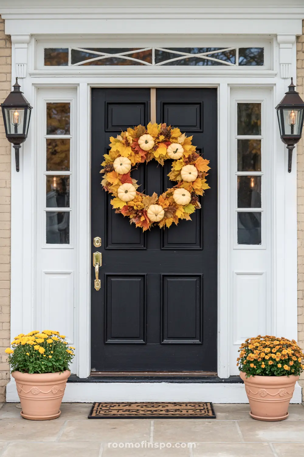 A beautiful fall wreath adorned with yellow leaves and small white pumpkins hangs on a black front door.