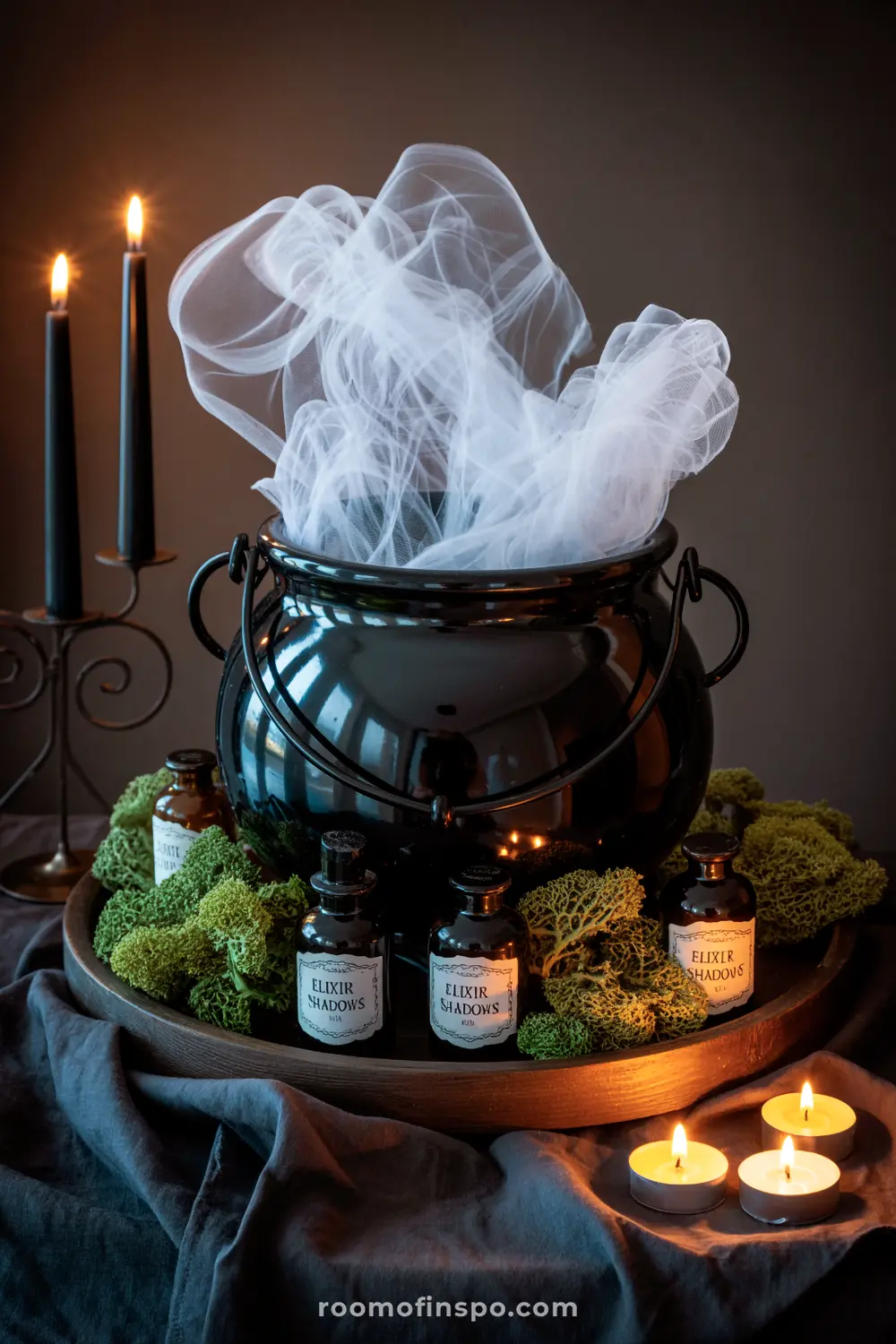 A spooky Halloween centerpiece with a black cauldron emitting white "smoke", surrounded by moss, potion bottles, and flickering candles.