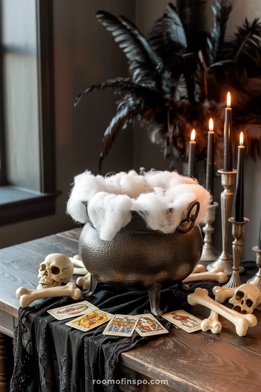 A mysterious Halloween centerpiece features a cauldron with faux smoke, surrounded by skulls, bones, and tarot cards on a black lace runner.