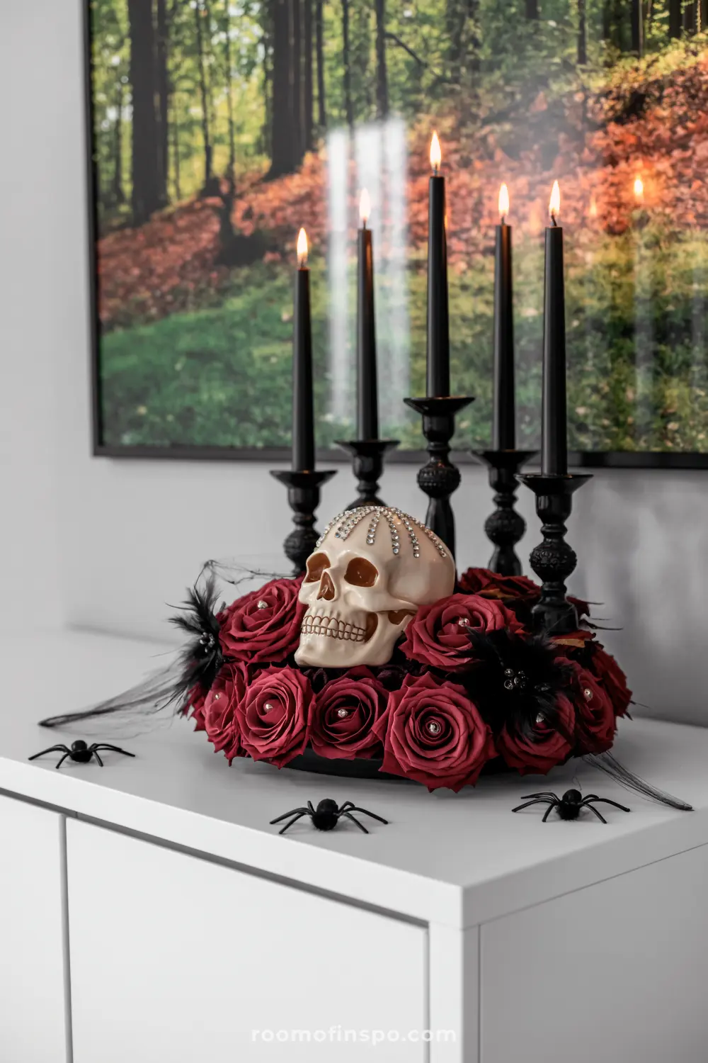 A dazzling Halloween centerpiece features a bejeweled skull nestled among deep red roses, surrounded by black candles and scattered spiders.