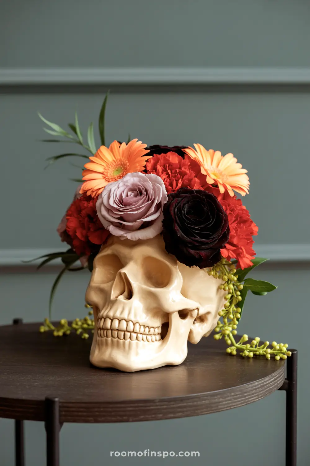 A vibrant Halloween centerpiece showcasing a skull with an arrangement of colorful flowers, including orange, red, purple, and black blooms.