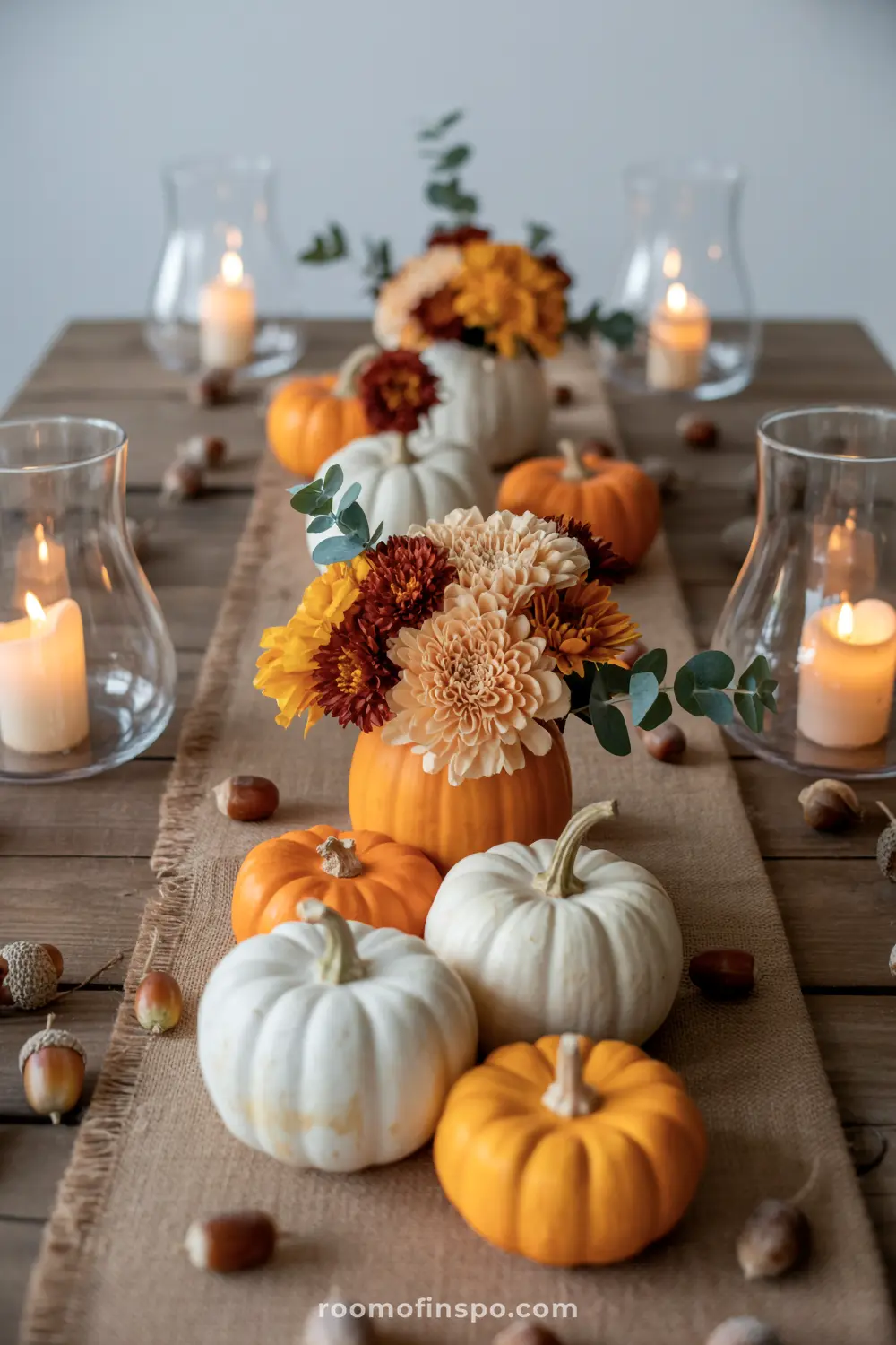 A charming Halloween centerpiece featuring a table runner with various pumpkins, fall flowers, and candles in glass holders.