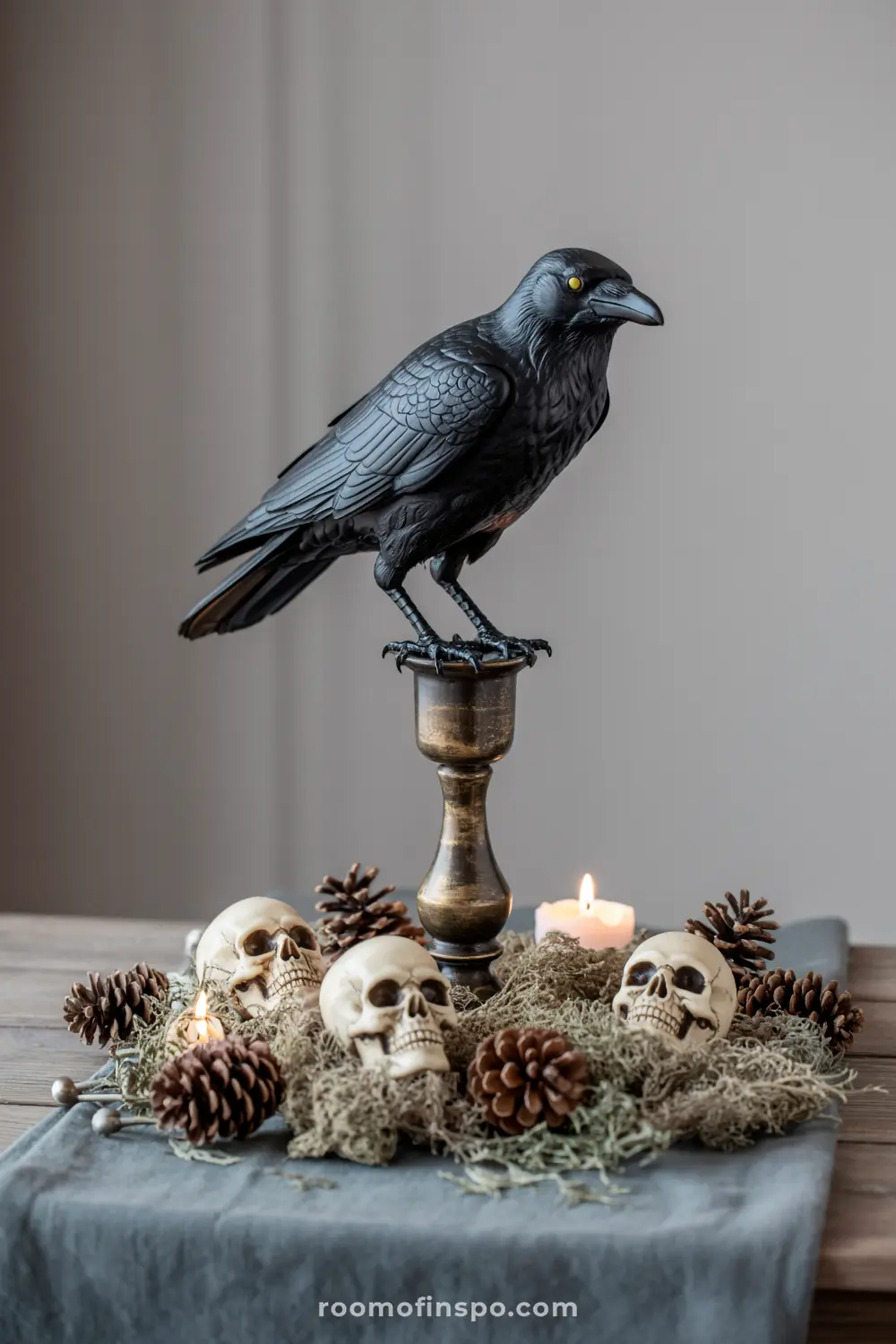 A captivating Halloween centerpiece with a black crow perched on a candlestick, surrounded by skulls, moss, pinecones, and a flickering tea light.
