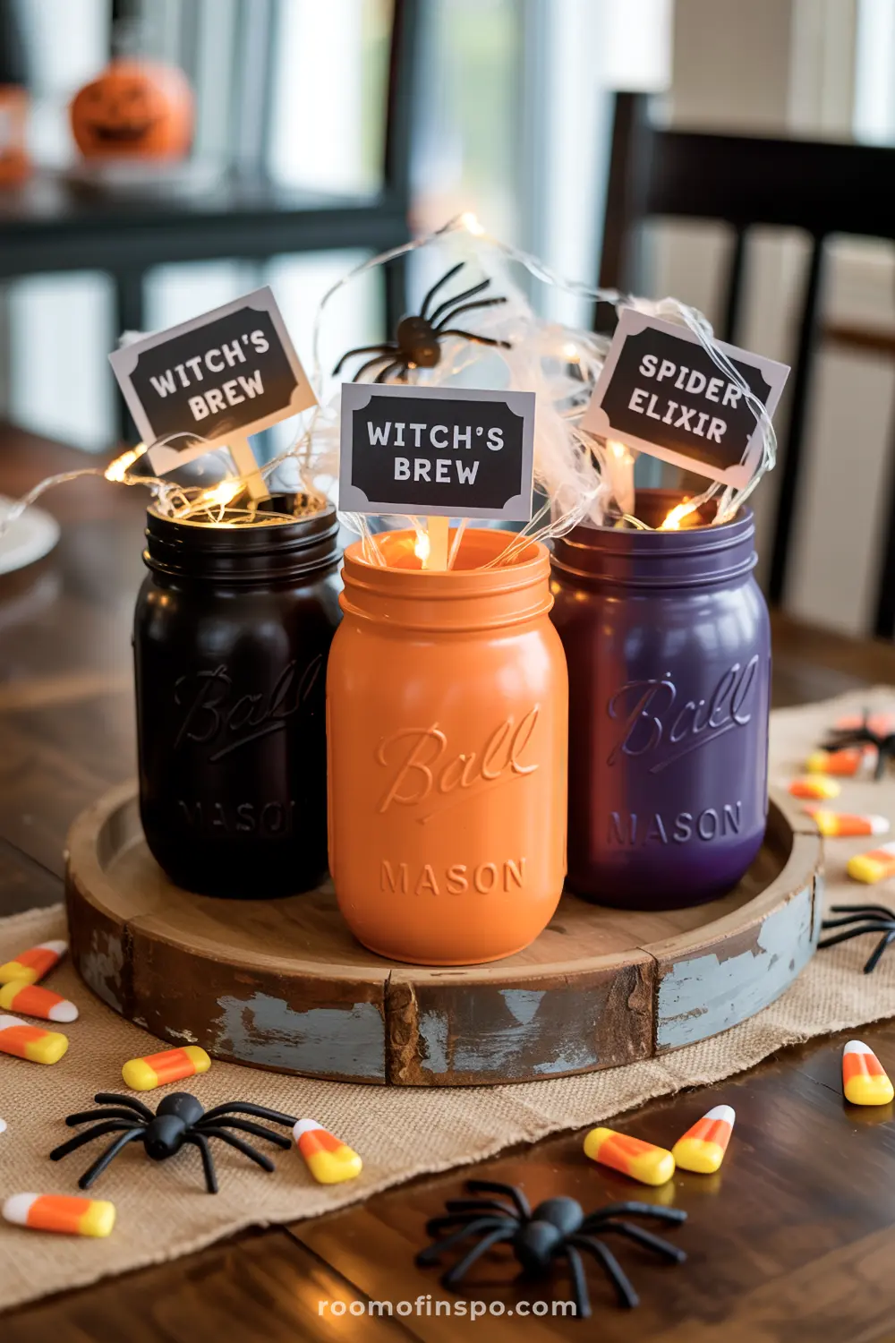 A playful Halloween centerpiece featuring black, orange, and purple mason jars with "Witch's Brew" signs, surrounded by candy corn and spiders.
