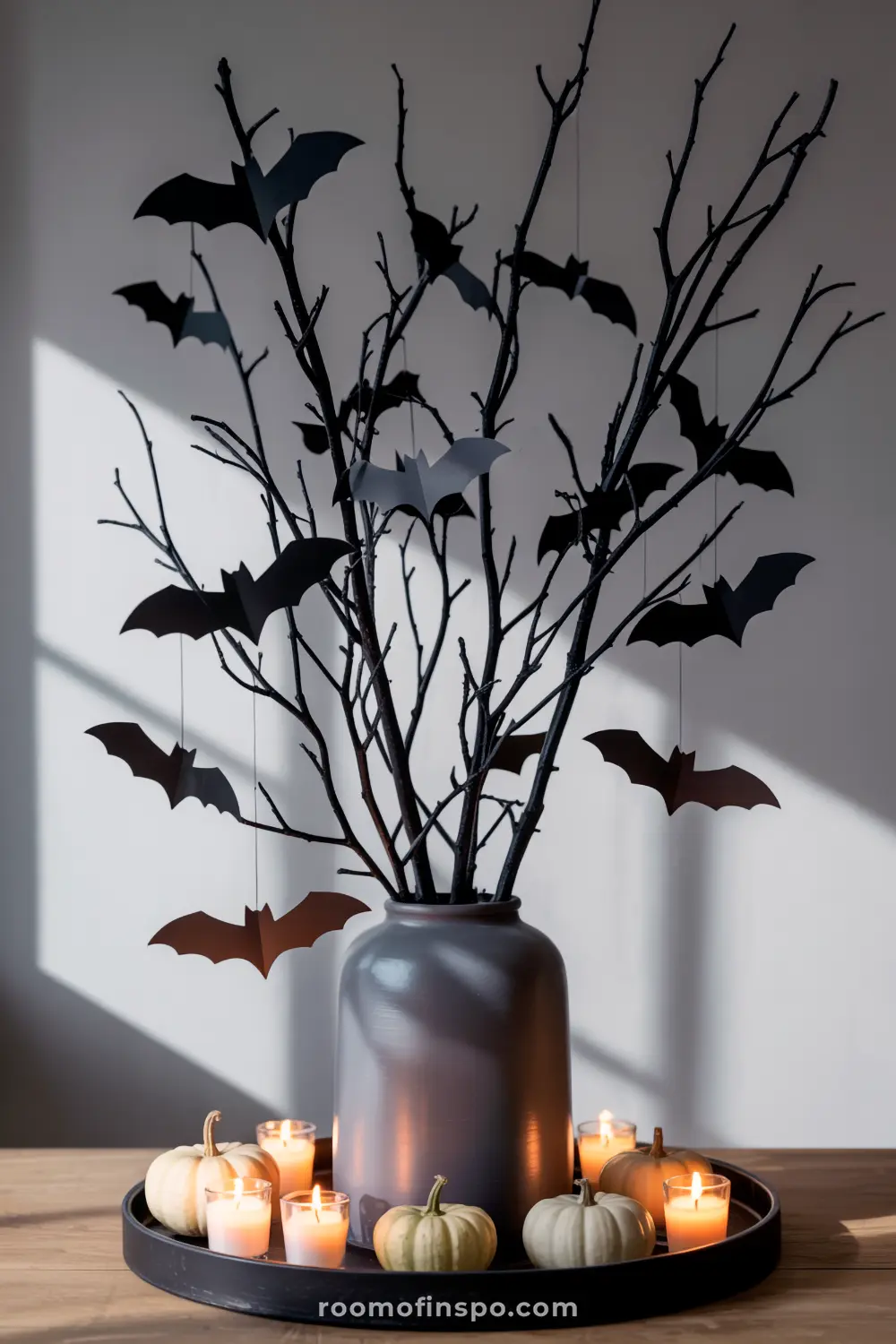 A dramatic Halloween centerpiece features bare branches in a vase with hanging bats, surrounded by mini pumpkins and flickering candles.