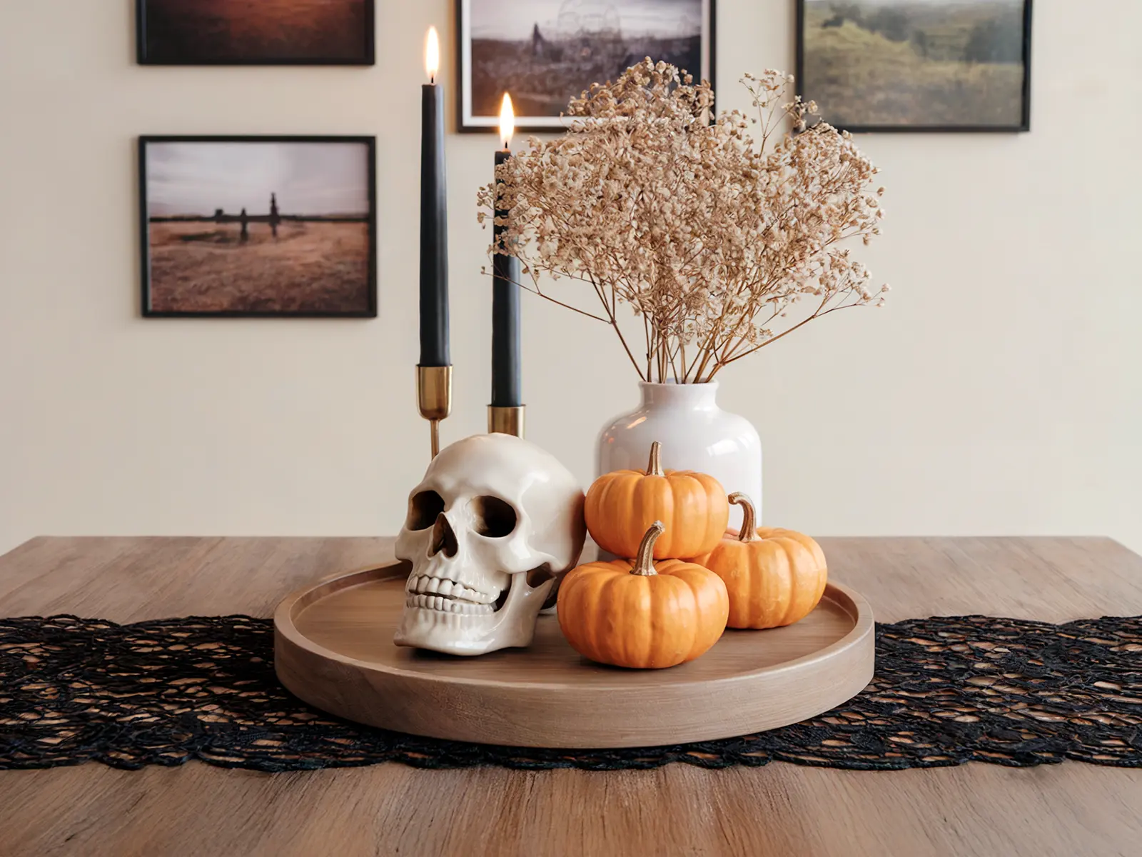 A Halloween centerpiece features a skull, mini pumpkins, and dried flowers on a wooden tray with a black lace runner.