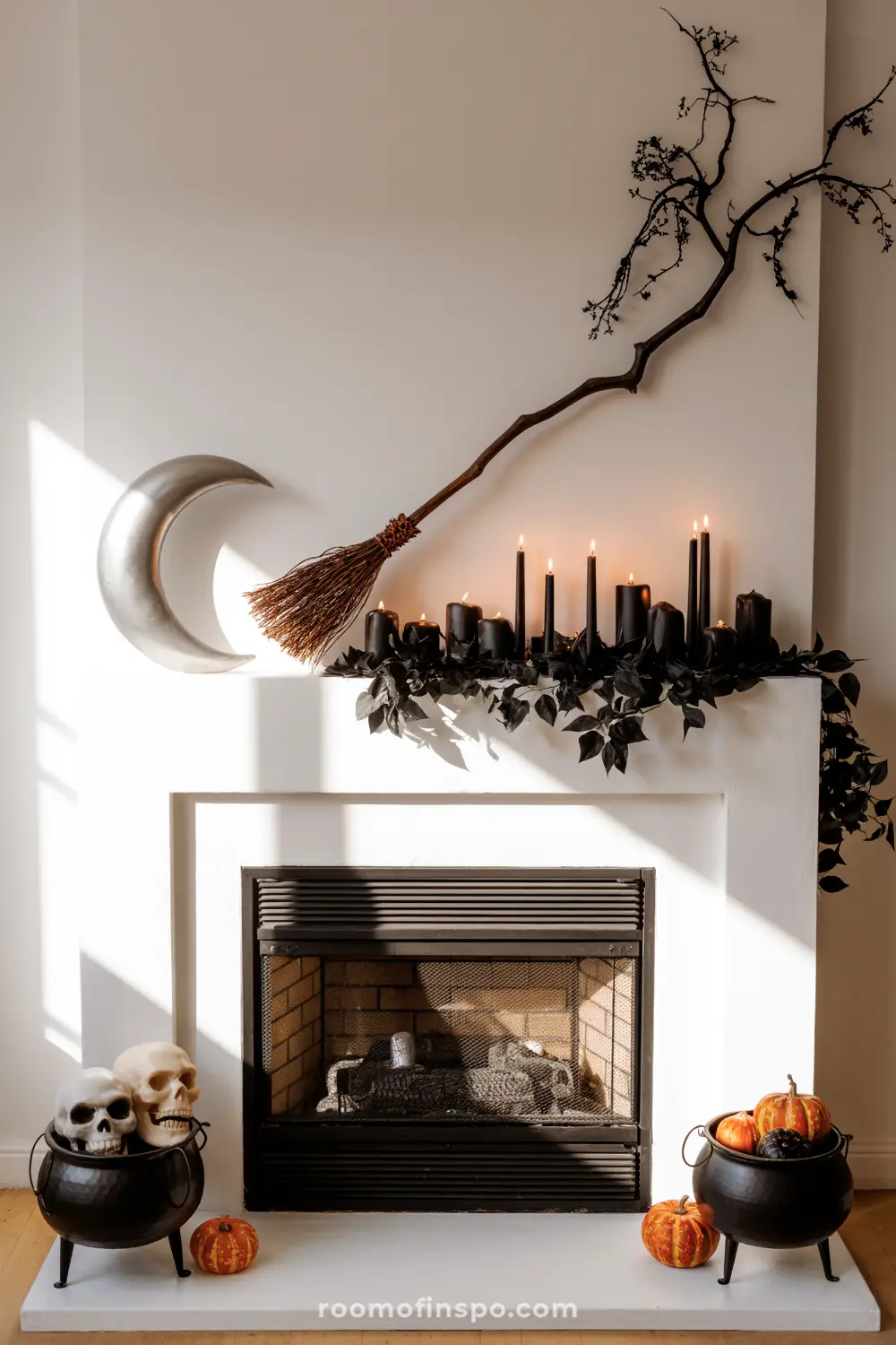 A spooky Halloween mantel features black candles, dark foliage, a broom, and a moon, with skulls and pumpkins in cauldrons below.