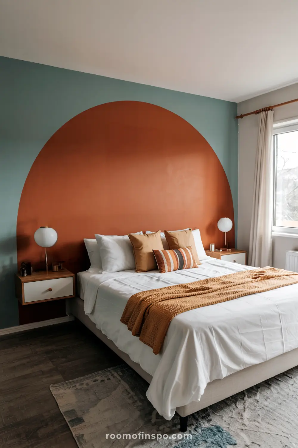 A modern bedroom with a headboard-free bed, white bedding, multiple beige and brown pillows, a large burnt-orange semi-circle accent on a teal wall, two white nightstands with wooden accents, spherical white lamps, a window with white curtains, and a patterned rug.