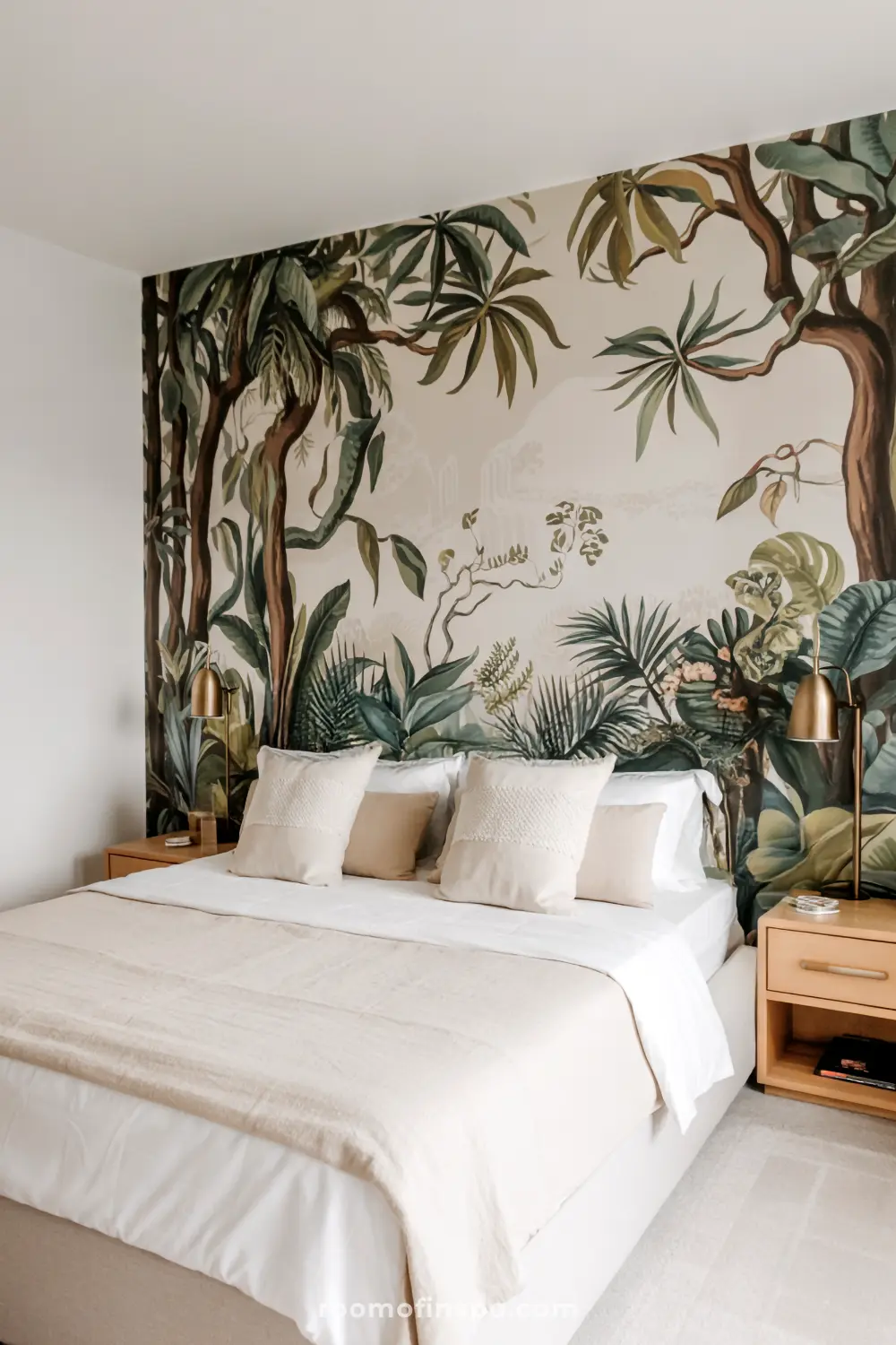 A stylish bedroom with a headboard-free bed featuring white and beige linens, a gold-framed tropical mural on the wall, two wooden nightstands with gold-colored lamps, and a warm neutral color palette.
