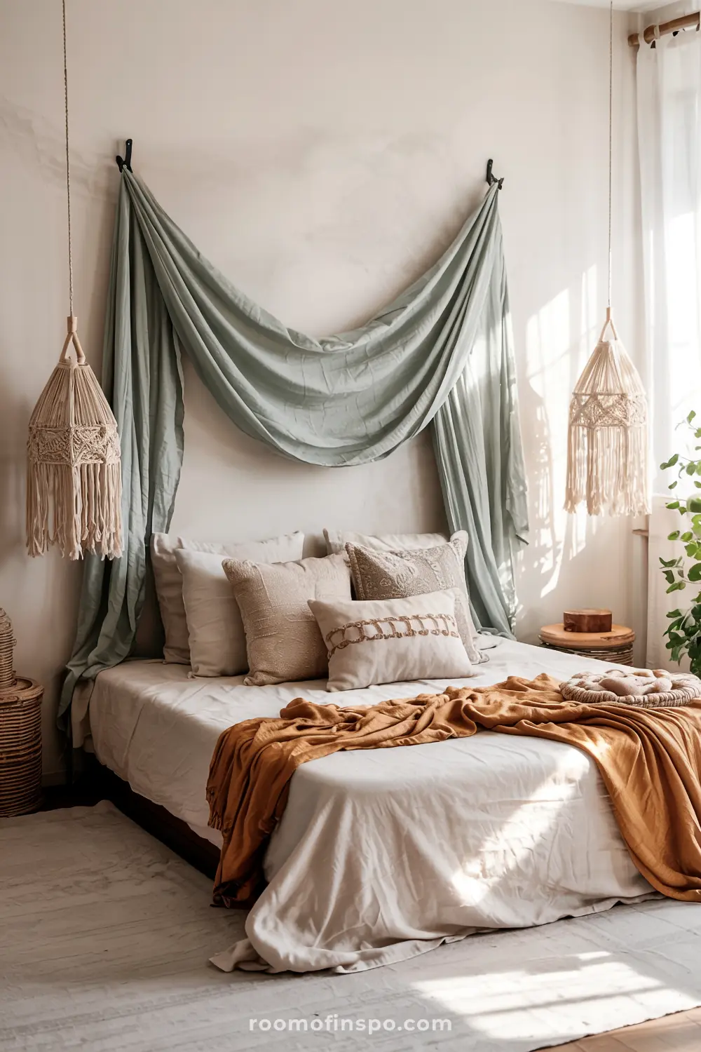A cozy bedroom with a headboard-free bed featuring white and beige linens, a mustard-colored throw blanket, draped green fabric above the bed, macrame hanging lamps, a small wooden side table with a plant, and a warm bohemian ambiance.