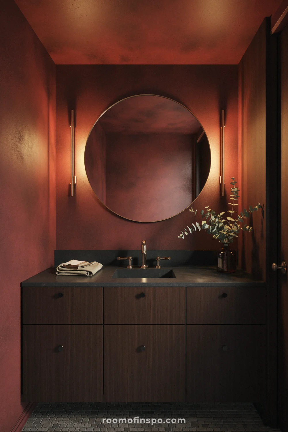 Deep red powder room with walnut vanity, black stone counter, brass mirror, and warm sconces.
