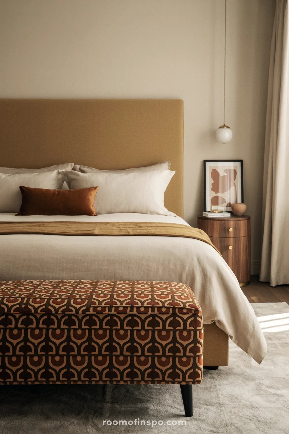Bedroom with retro patterned ottoman, neutral headboard, rust velvet throw, walnut nightstands, and linen curtains.