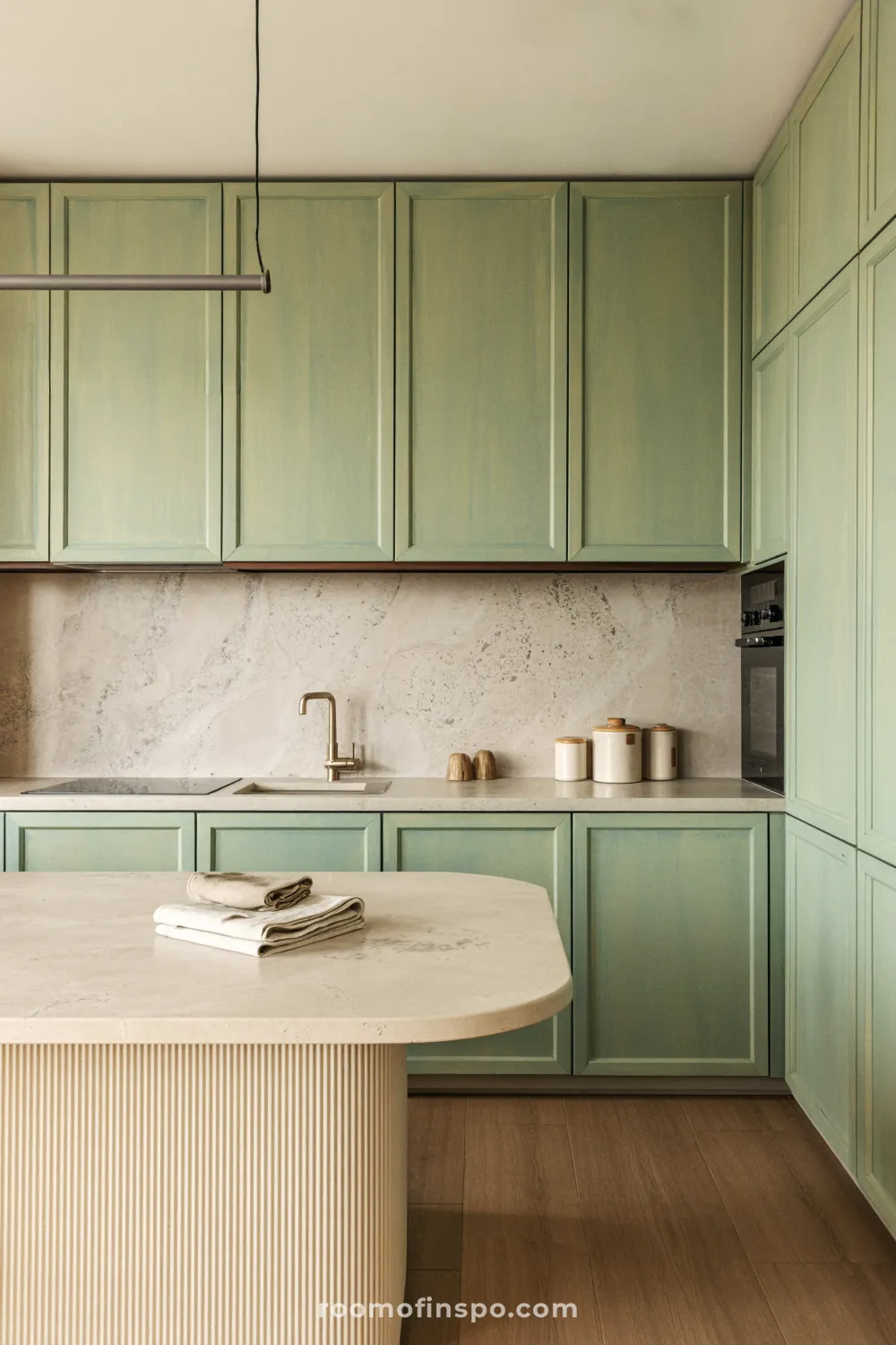 The modern kitchen incorporates green-hued matte cabinetry and light wood floors, creating a sophisticated and natural feel.
