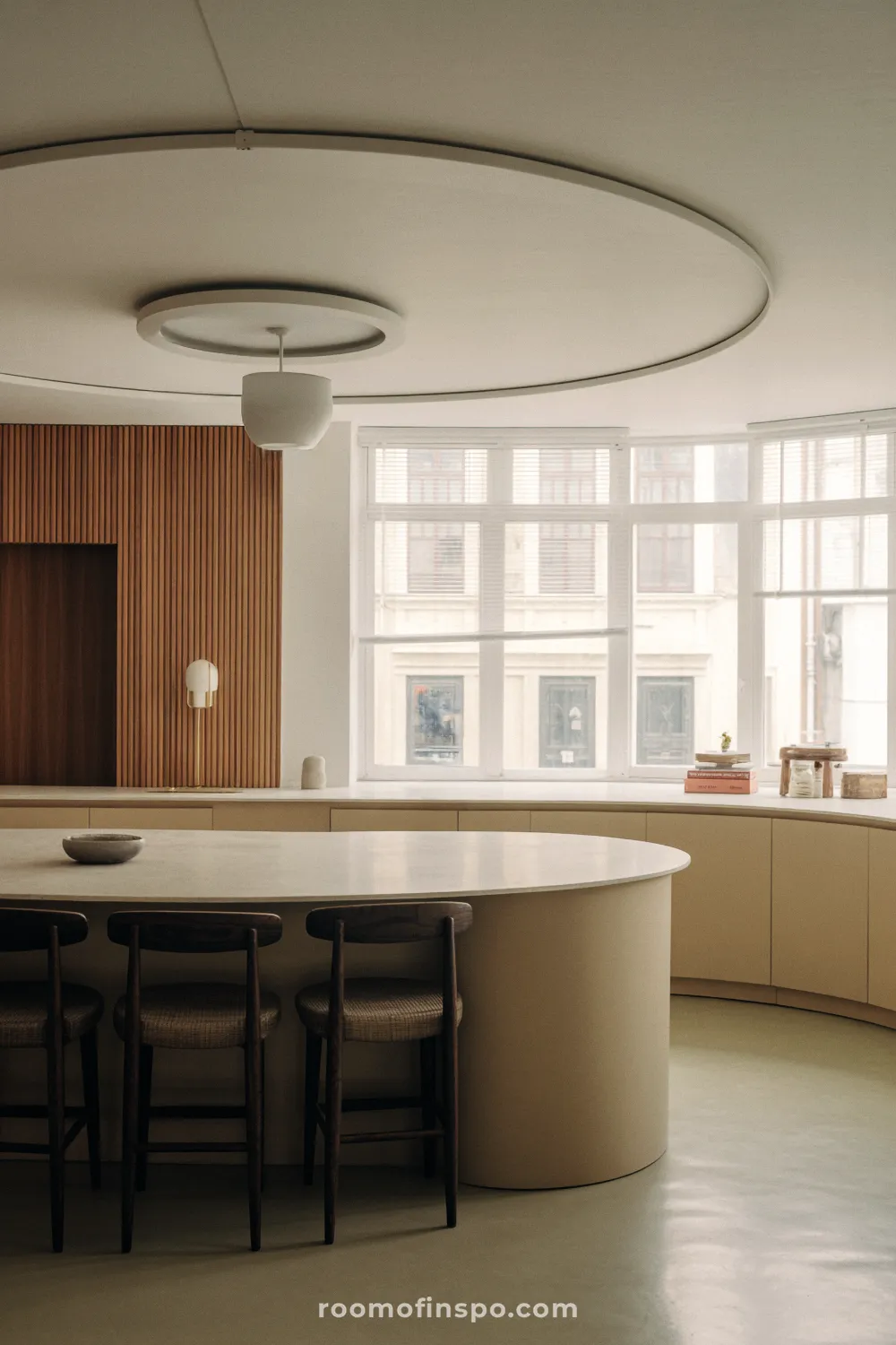 A bright, minimalist kitchen with a dining area featuring curved details on the island and windows for a gentle feel.