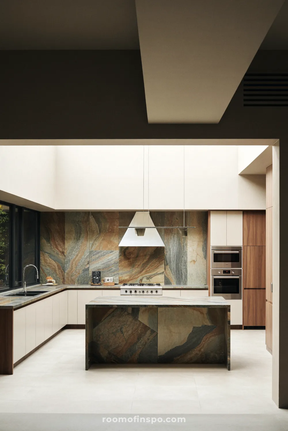 This sleek kitchen design uses light wood and a continuous, dark stone slab for the countertop and backsplash area.