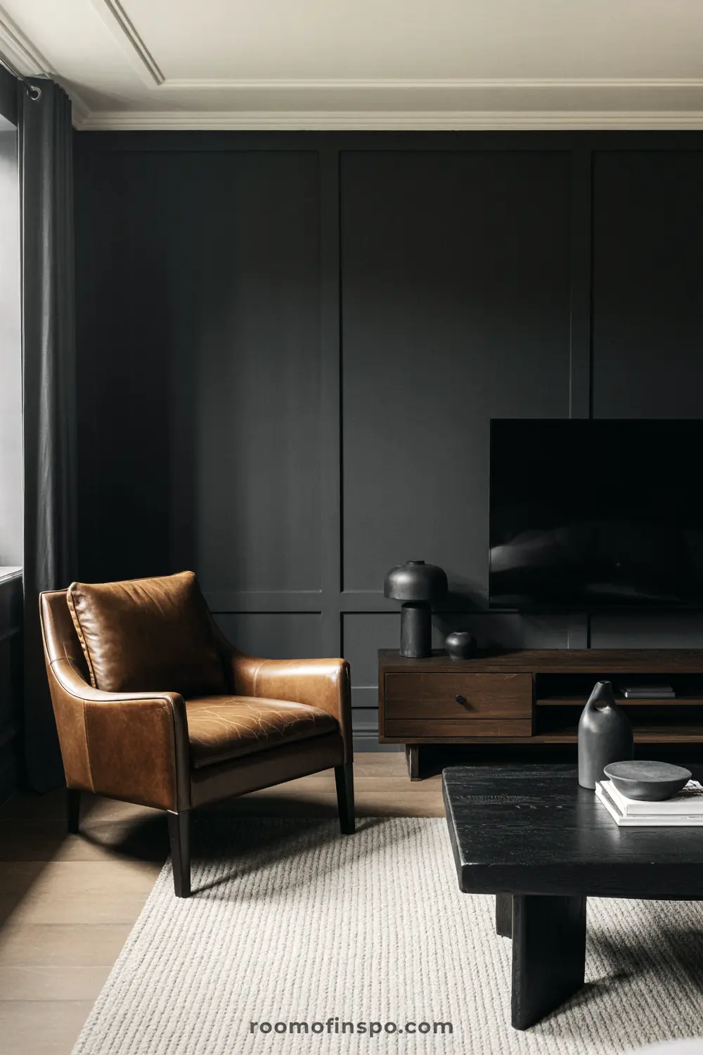 A moody, dark, masculine living room with a brown leather armchair and a black, low-profile coffee table.