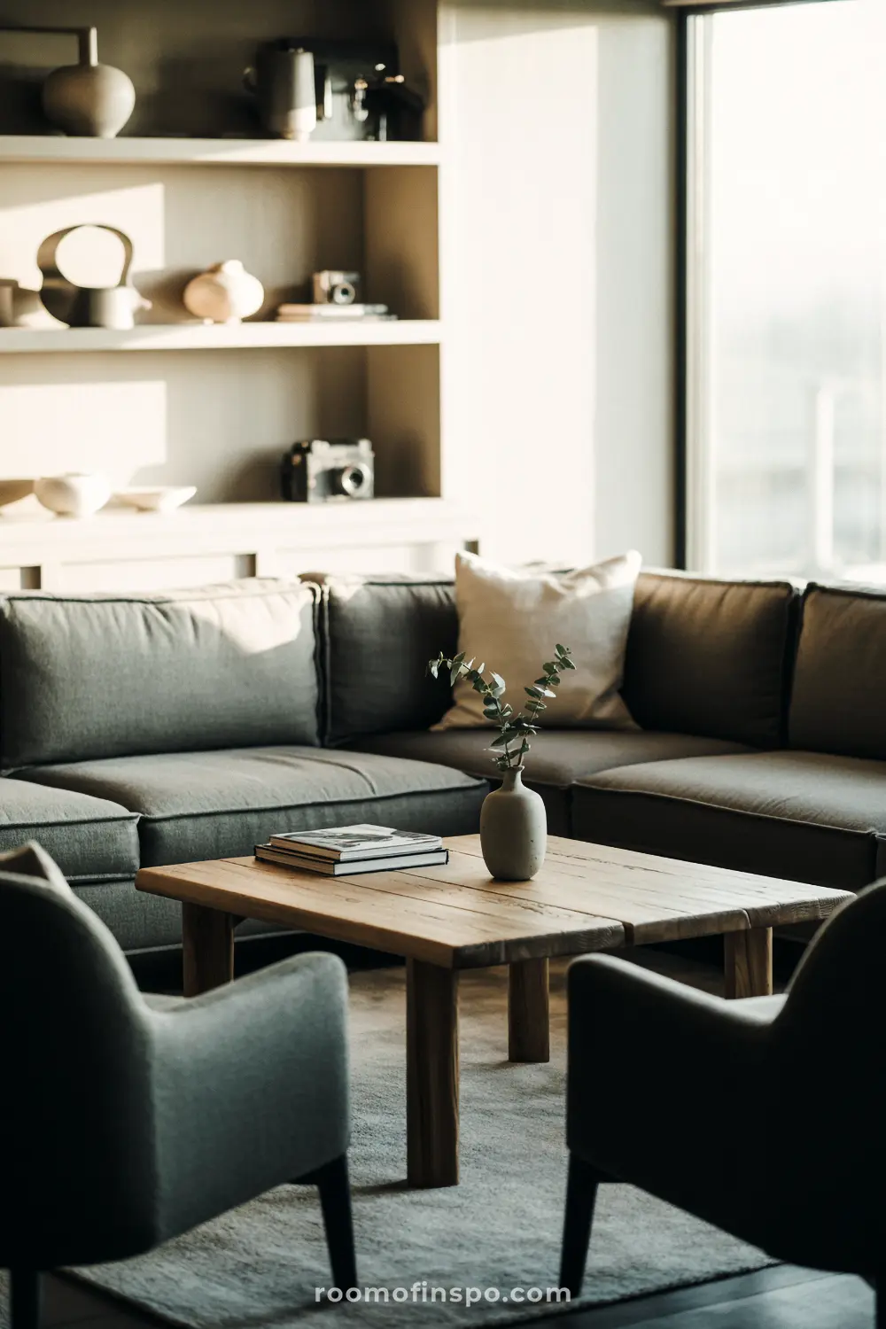 A modern masculine living room with a gray sectional sofa, a wooden coffee table, and an open shelf with vases.