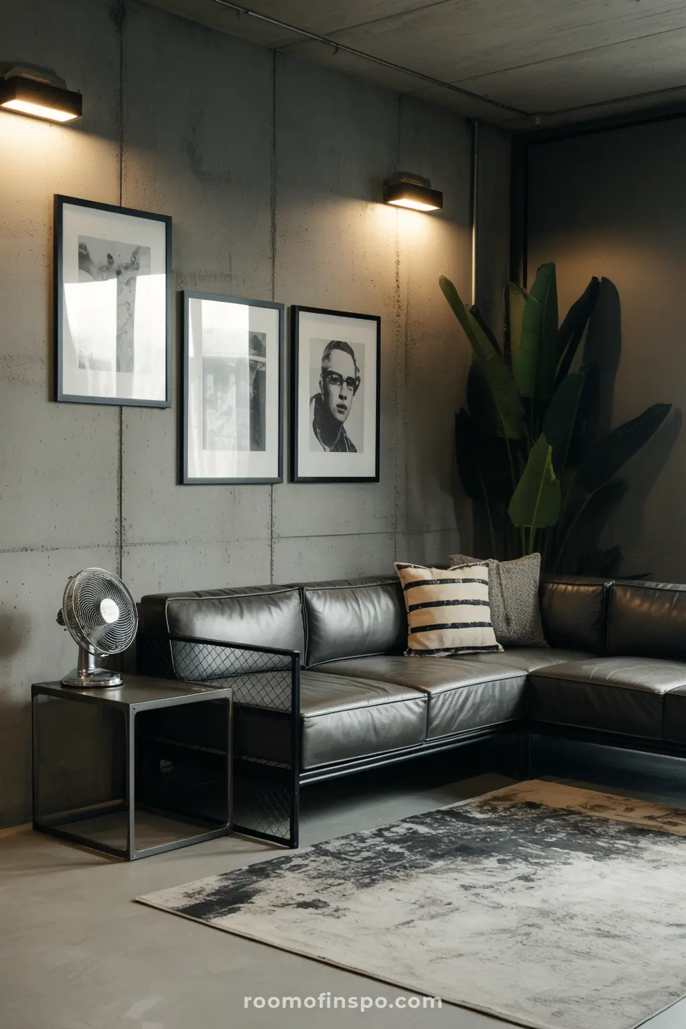 A dark and masculine living room with a gray sectional sofa, concrete walls, and three framed pictures hanging above the sofa.