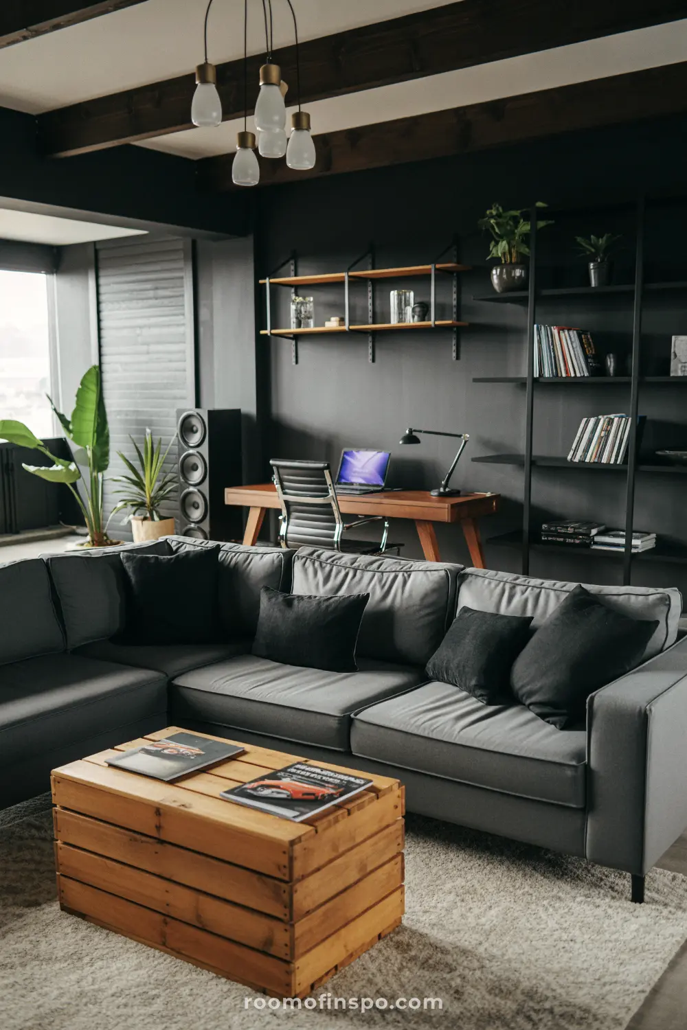 A man's industrial-style living room with a gray sectional sofa, a wooden crate coffee table, and an office desk behind it.