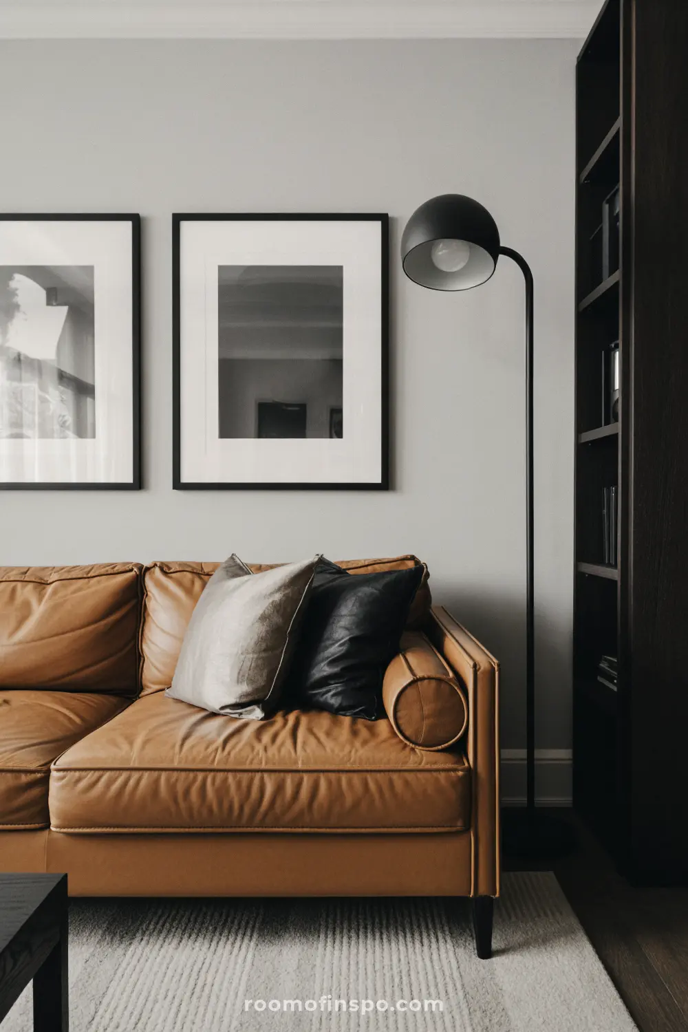 A stylish masculine living room with a brown leather sofa, two framed pictures, and a tall black floor lamp.