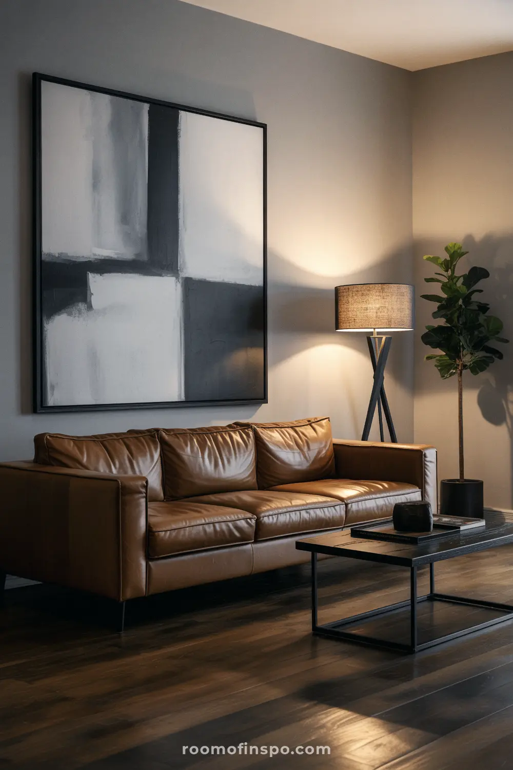A stylish man's living room with a brown leather sofa, an abstract painting, and a black coffee table.