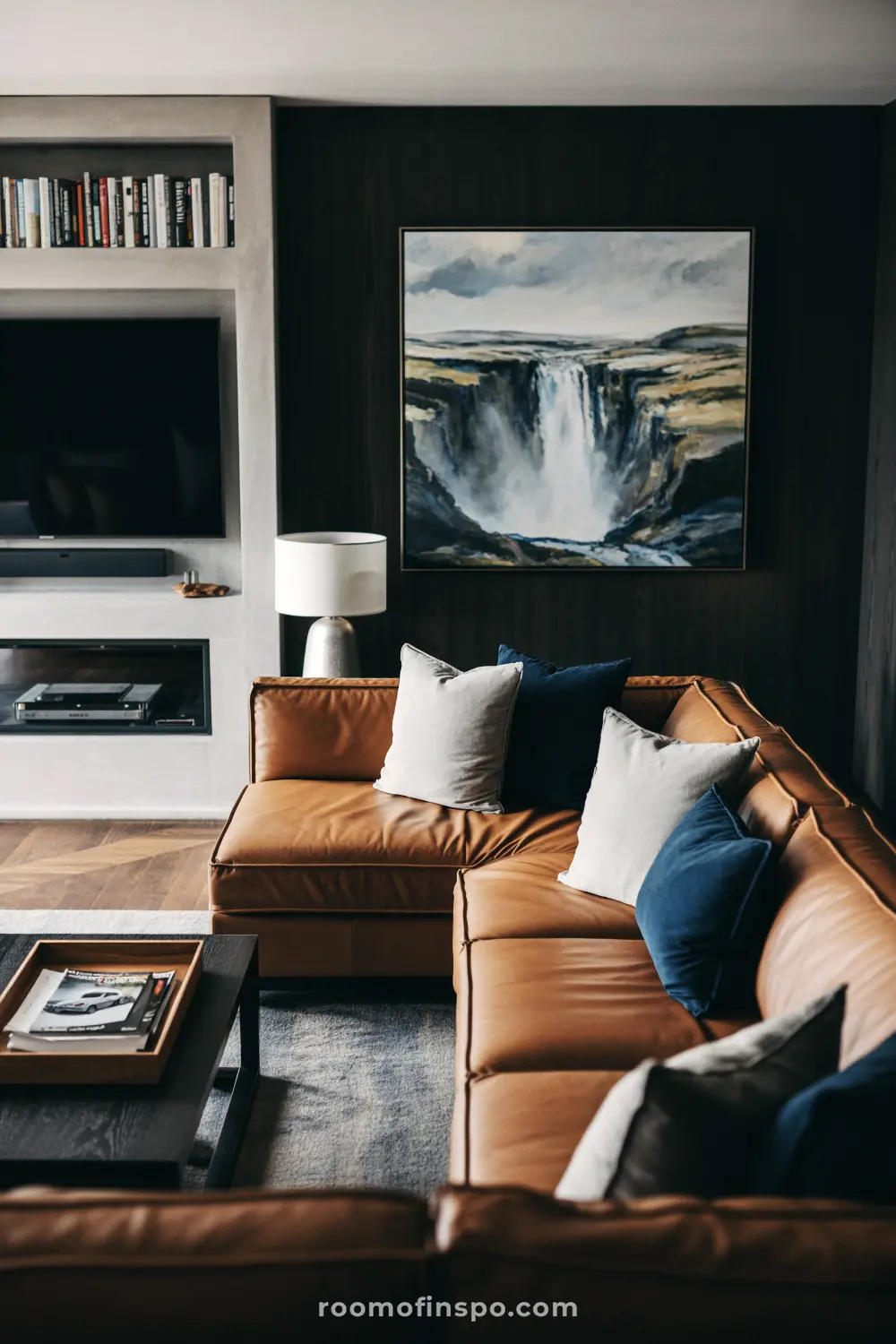 A sophisticated man's living room with a brown leather sofa, a waterfall painting, and a white, built-in media console.