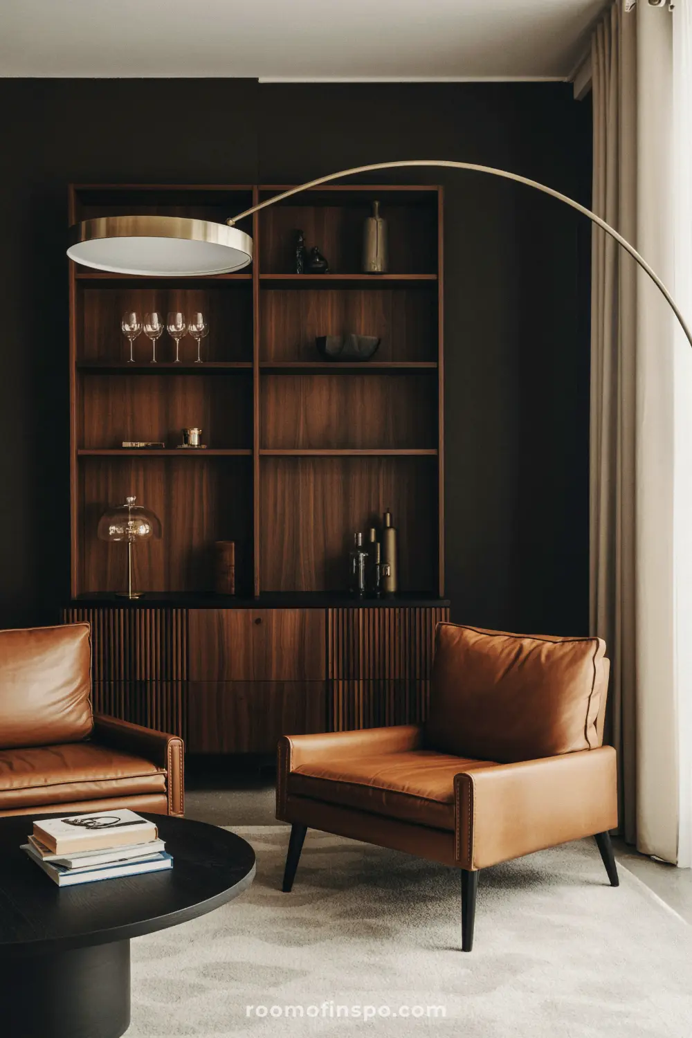 A masculine living room with a bar cabinet, two brown leather armchairs, a round table, and a unique floor lamp.