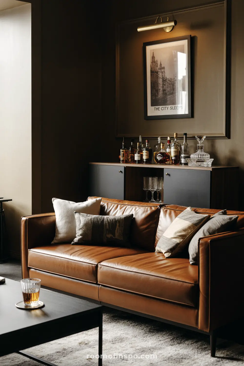 A masculine living room with a brown leather sofa, a well-stocked bar cabinet, and a framed picture above the cabinet.