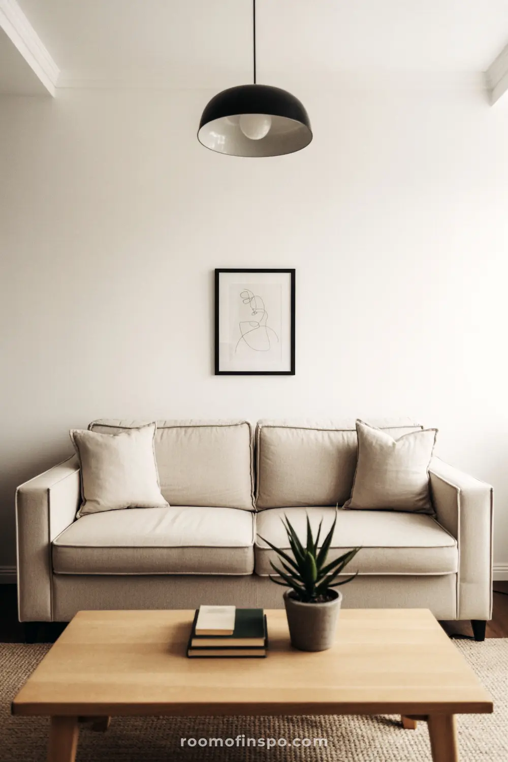 A clean, minimalist masculine living room with a white sofa, a wooden coffee table, and a large black light fixture.