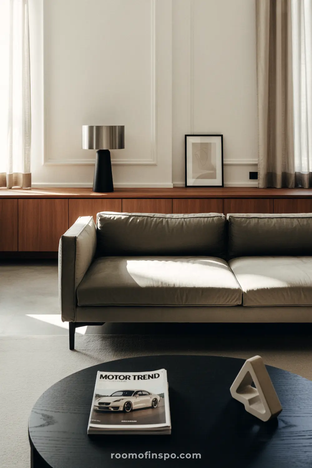 A masculine living room with a light gray sofa, a large brown cabinet, and a black circular coffee table.