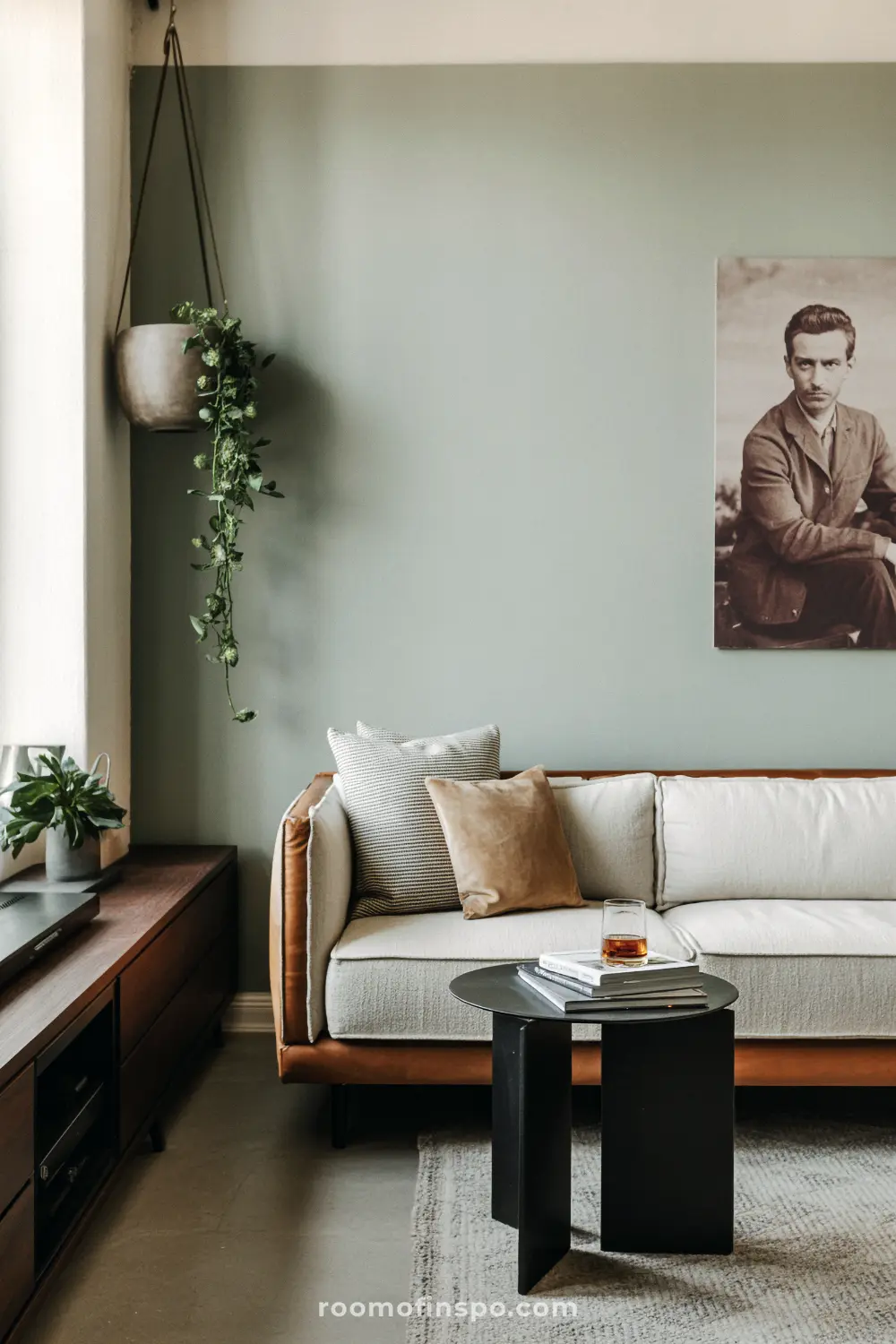 A masculine living room with a sage green wall, a brown and white sofa, a black table, and a portrait of a man.