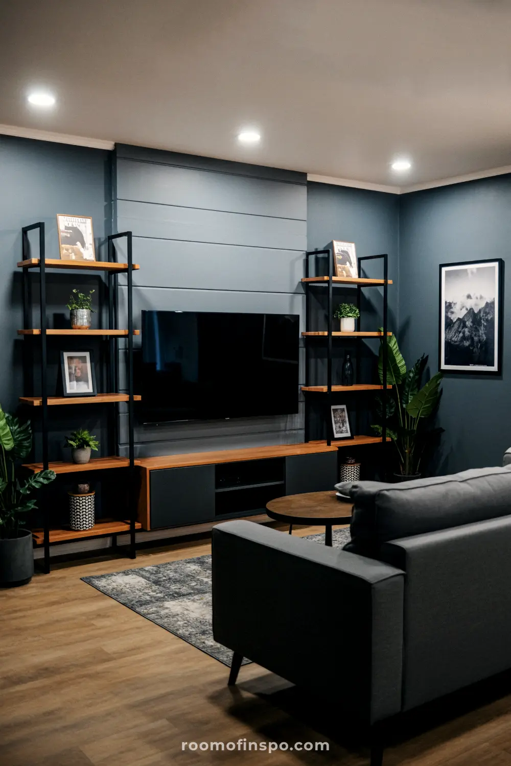A dark blue and masculine living room with a gray sofa, a large TV, and two tall bookshelves on either side.