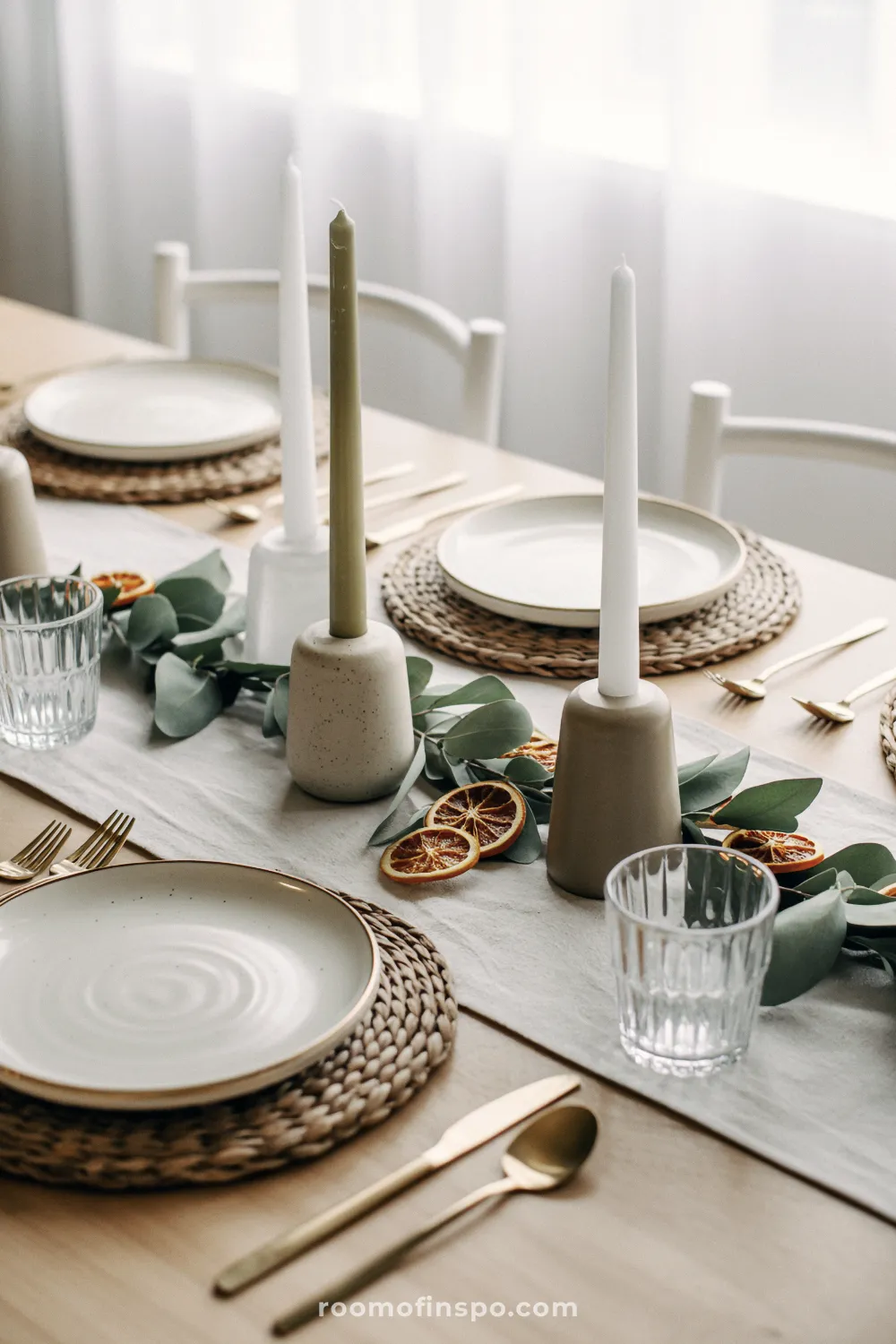 A minimalist Christmas tablescape features tall, slender candles and dried orange slices on a light runner.