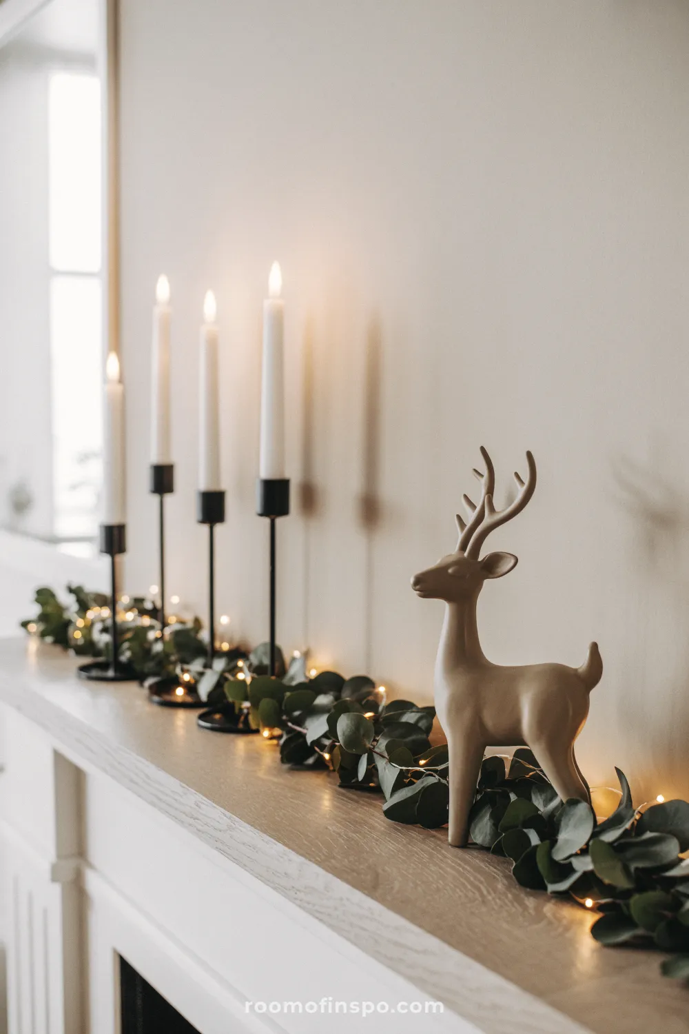 A mantle decorated with a neutral deer statue, eucalyptus garland, and candles for a minimalist Christmas display.