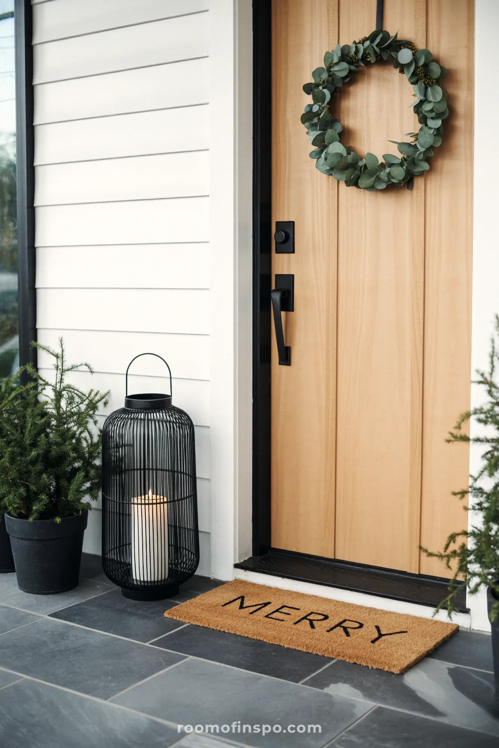 A simple front door features a eucalyptus wreath and a black lantern, offering a minimalist Christmas welcome.