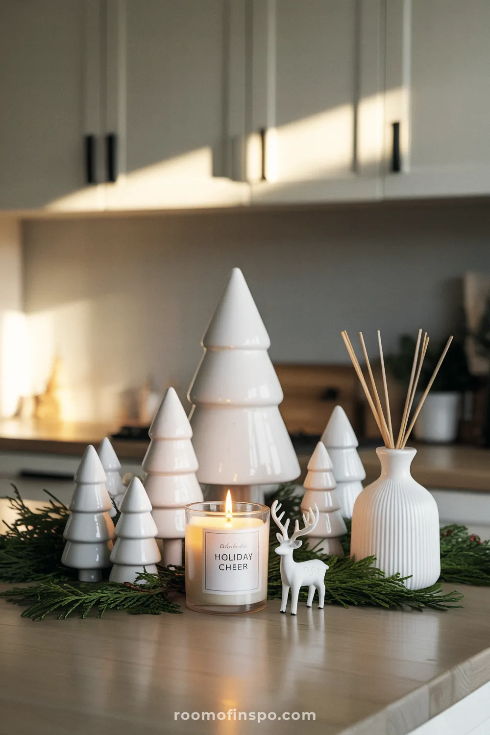 A cluster of white ceramic trees, a reindeer figurine, and a candle create a minimalist Christmas kitchen vignette.