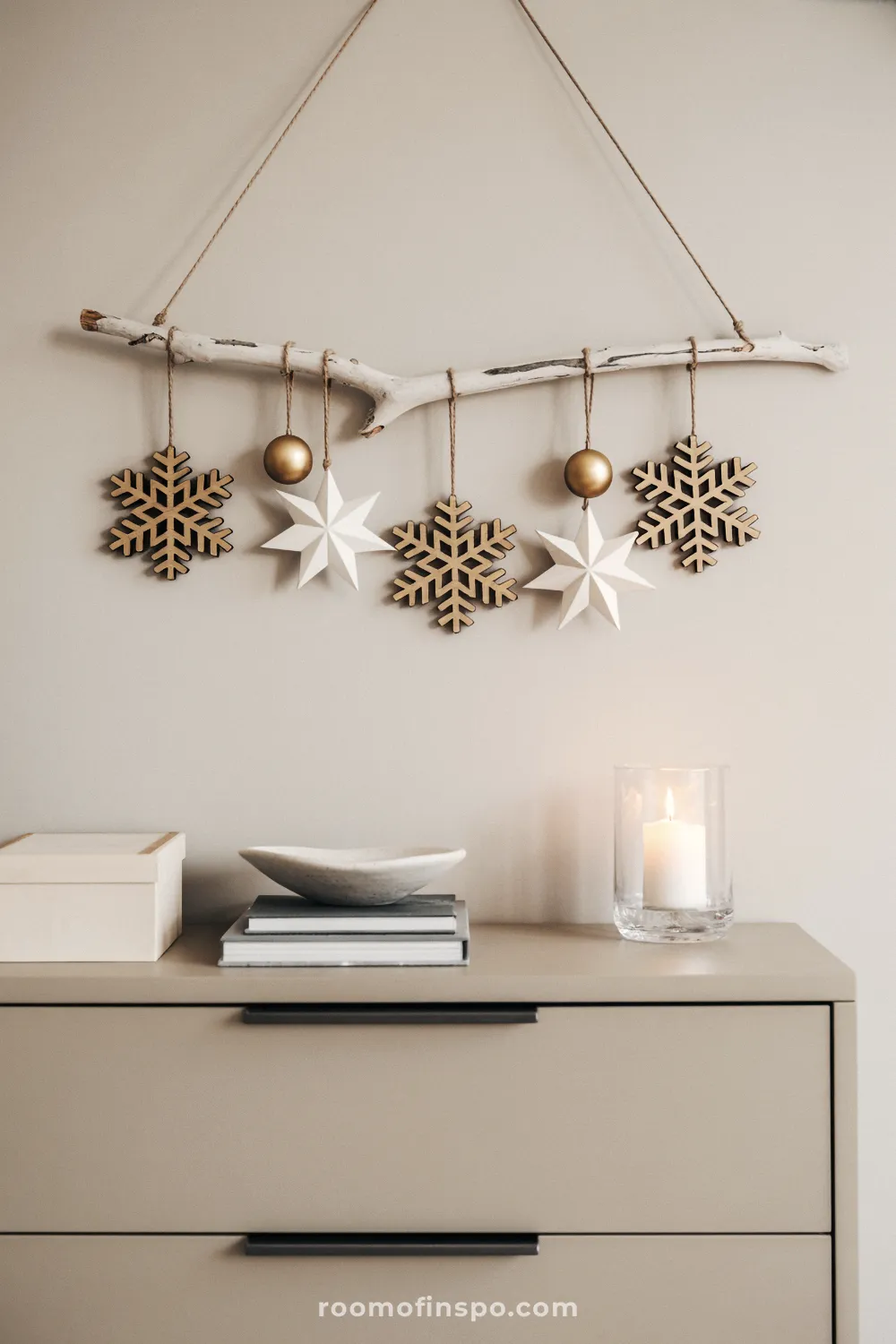 A branch hangs over a cabinet with wooden snowflakes and paper stars for a minimalist Christmas wall decor.