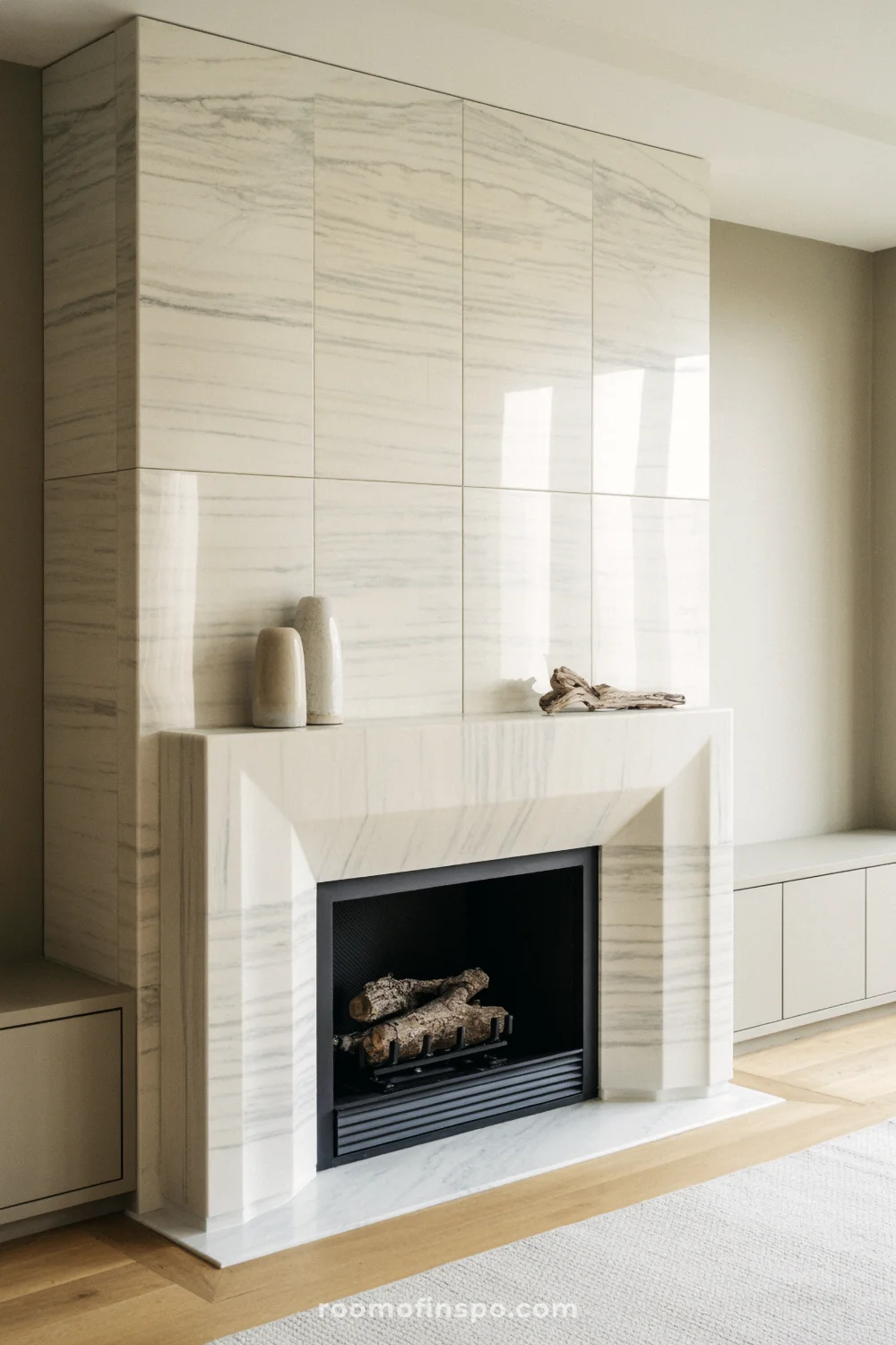 Bookmatched creamy marble fireplace with recessed ledge mantel, low black firebox, and pale greige cabinets.