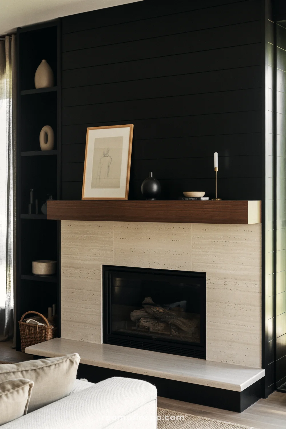Black shiplap fireplace wall with travertine surround and hearth, dark walnut mantel, and beige sofa in soft daylight.