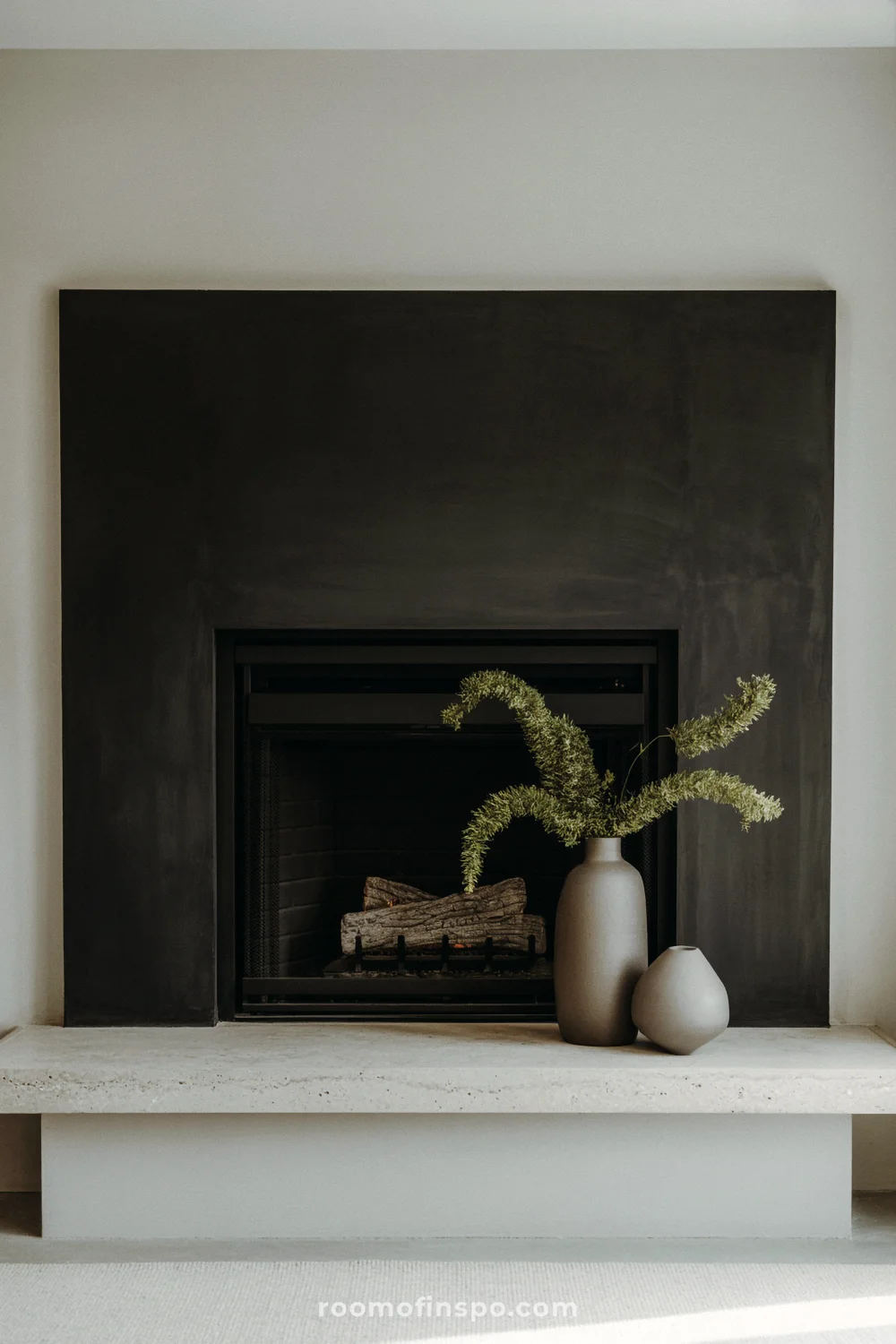 Dark charcoal fireplace surround with low wide firebox, light hearth, and ceramic vase with greenery.