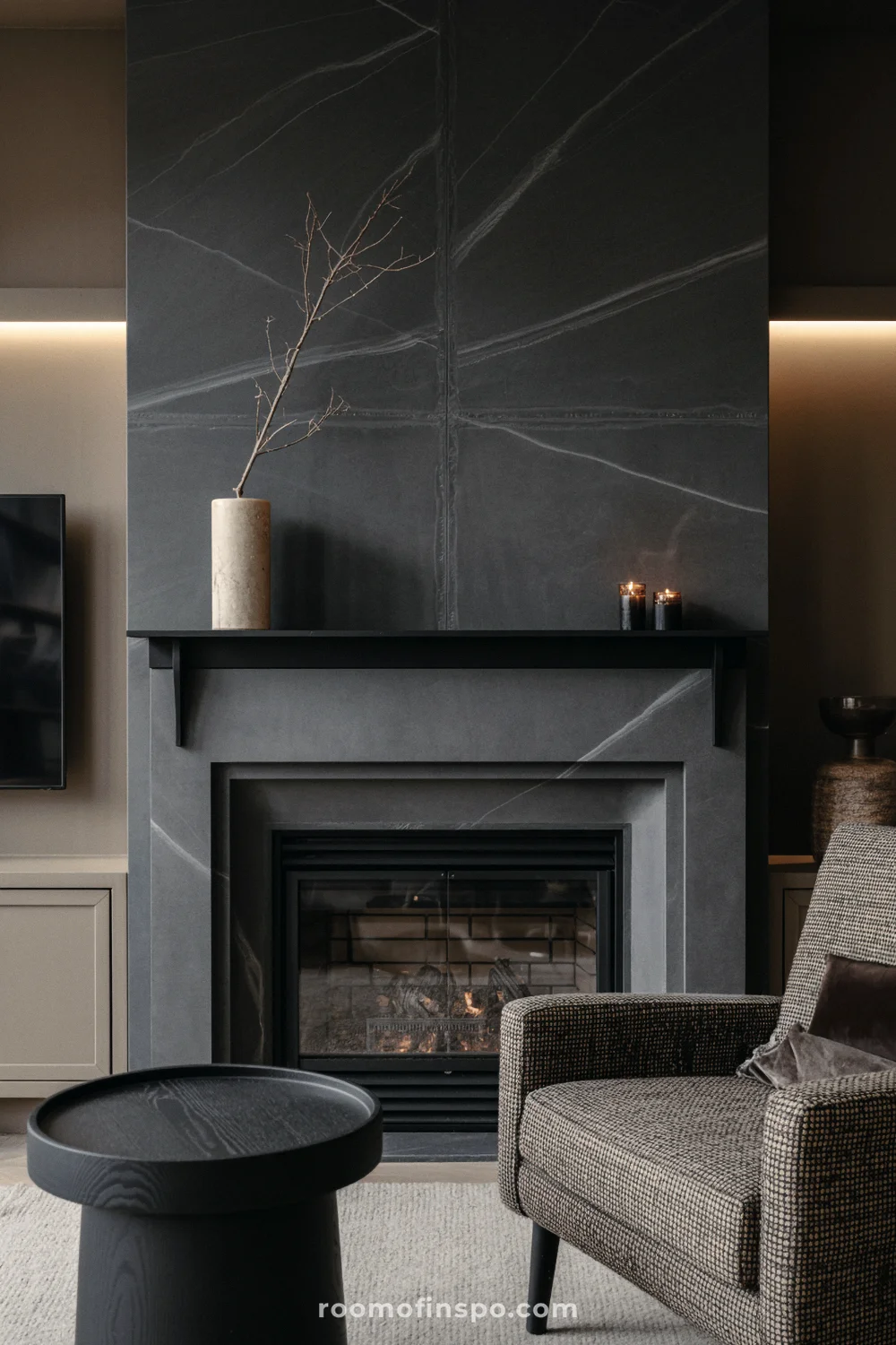 Charcoal soapstone fireplace with thin metal mantel, glass-front firebox, flax armchair, and greige built-ins.