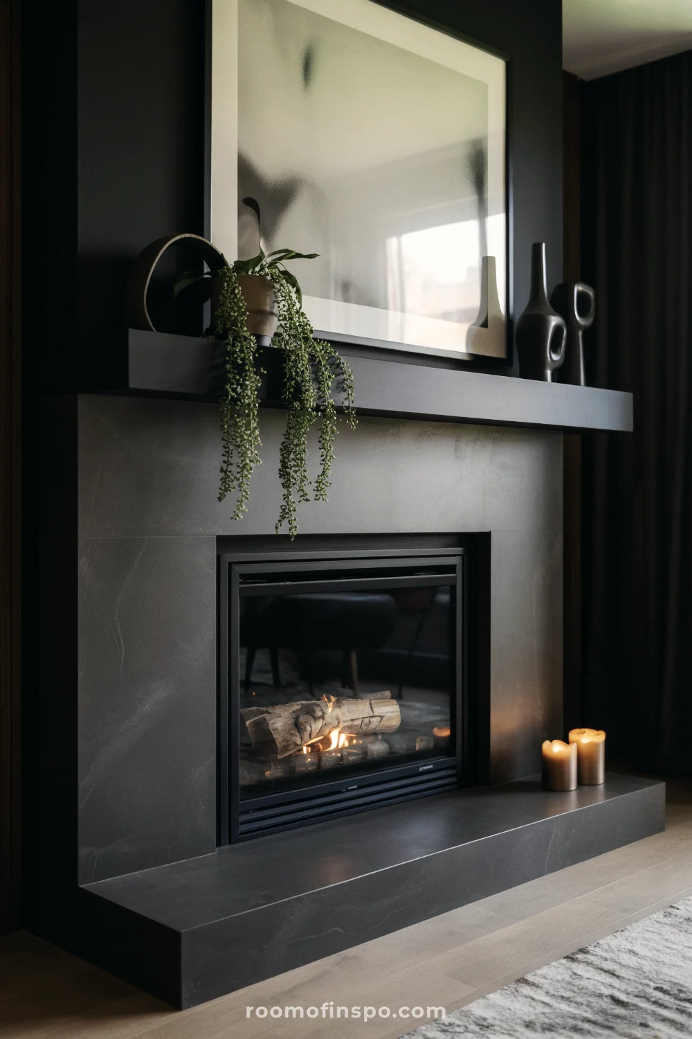 Matte black fireplace with slim linear firebox, abstract art above, candles and black vases, and light wood floors.