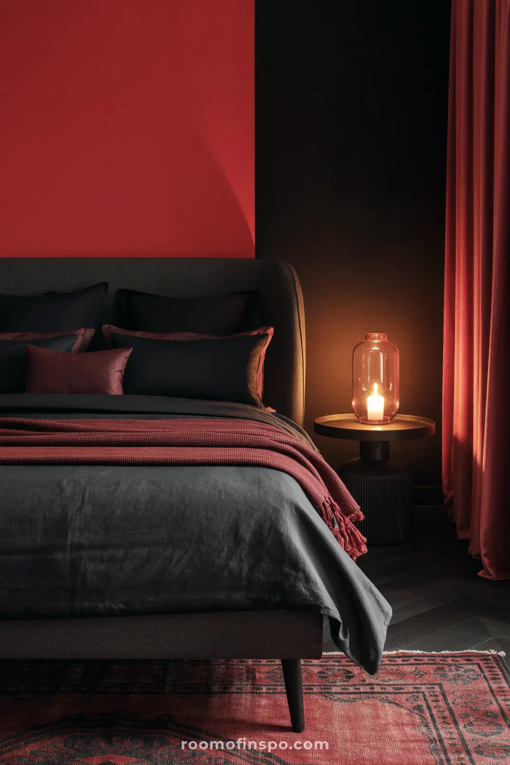 A dark and moody bedroom with a two-toned red and black wall, black and red bedding, and a single candlelit lantern.