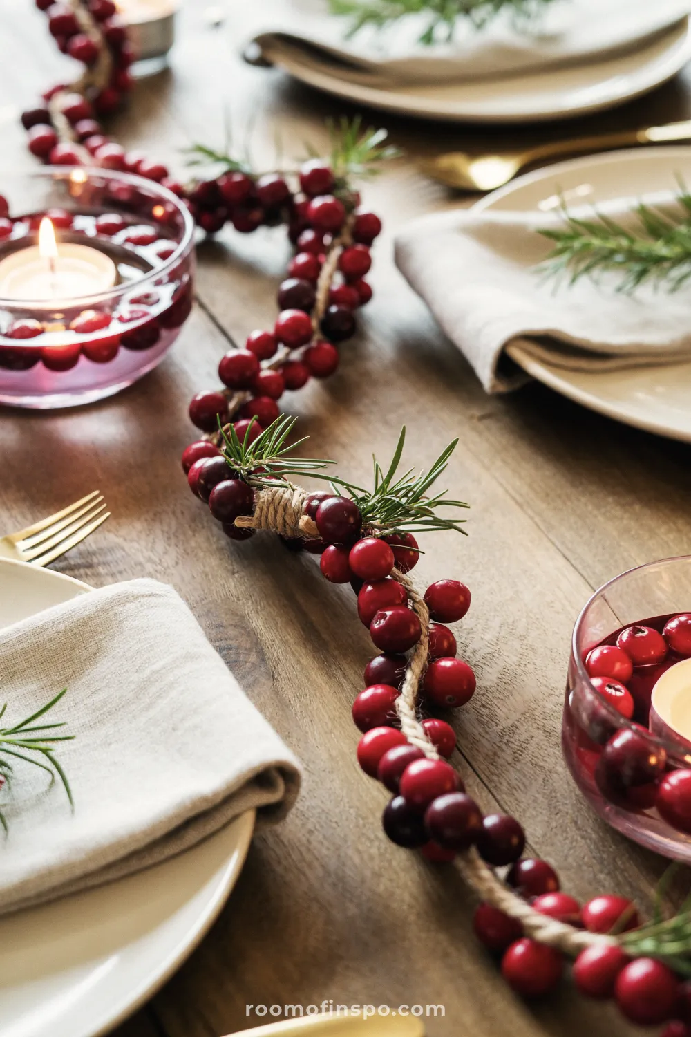 A dining table centerpiece uses a natural garland of cranberries and twine for a rustic yet elegant Christmas setting.