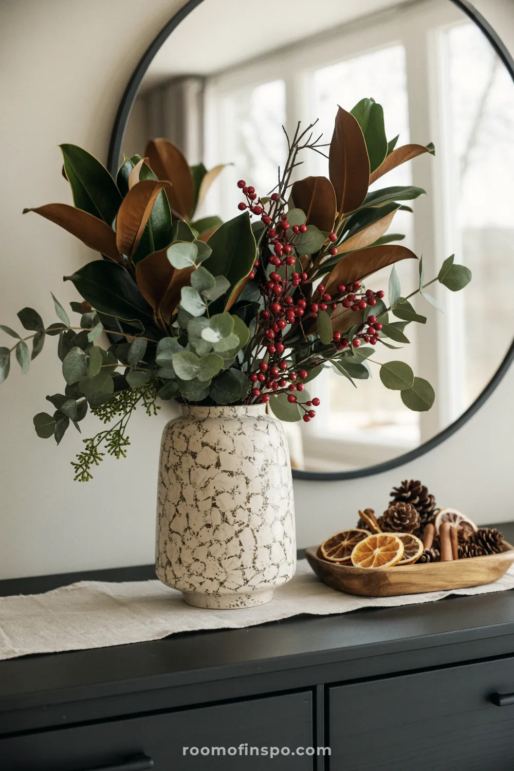 A textured vase holds a dramatic natural arrangement of magnolia, eucalyptus, and red berries for Christmas decor.