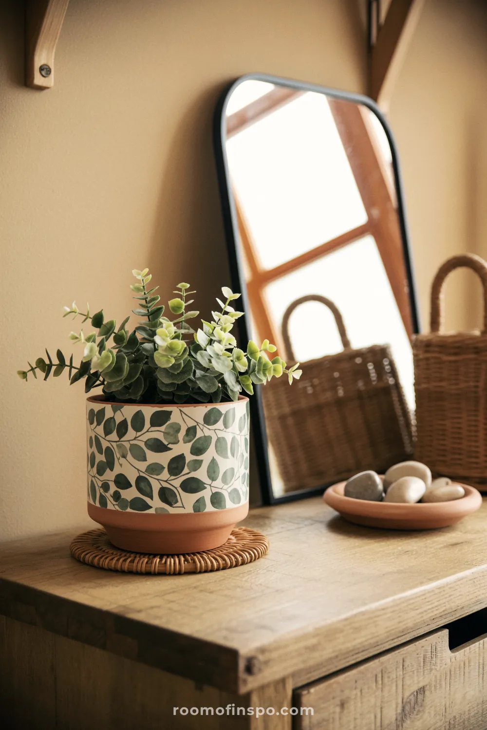 Vine-painted terracotta planter on a wooden console with rattan coaster, mirror, and woven basket nearby.