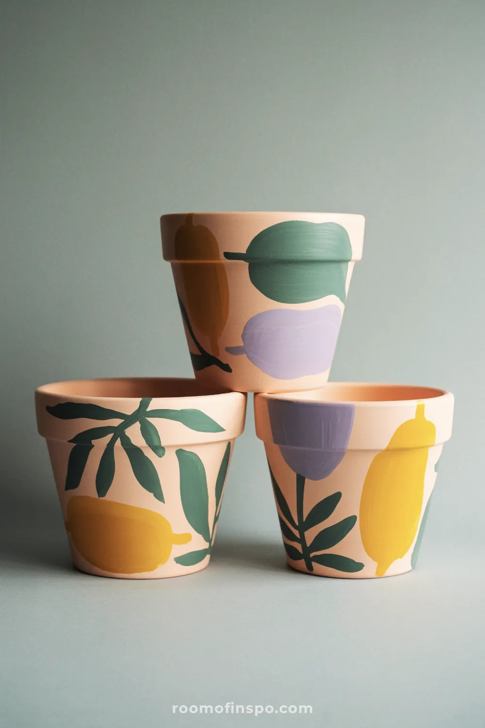 Three pastel botanical-painted terracotta pots arranged together against a light gray backdrop.