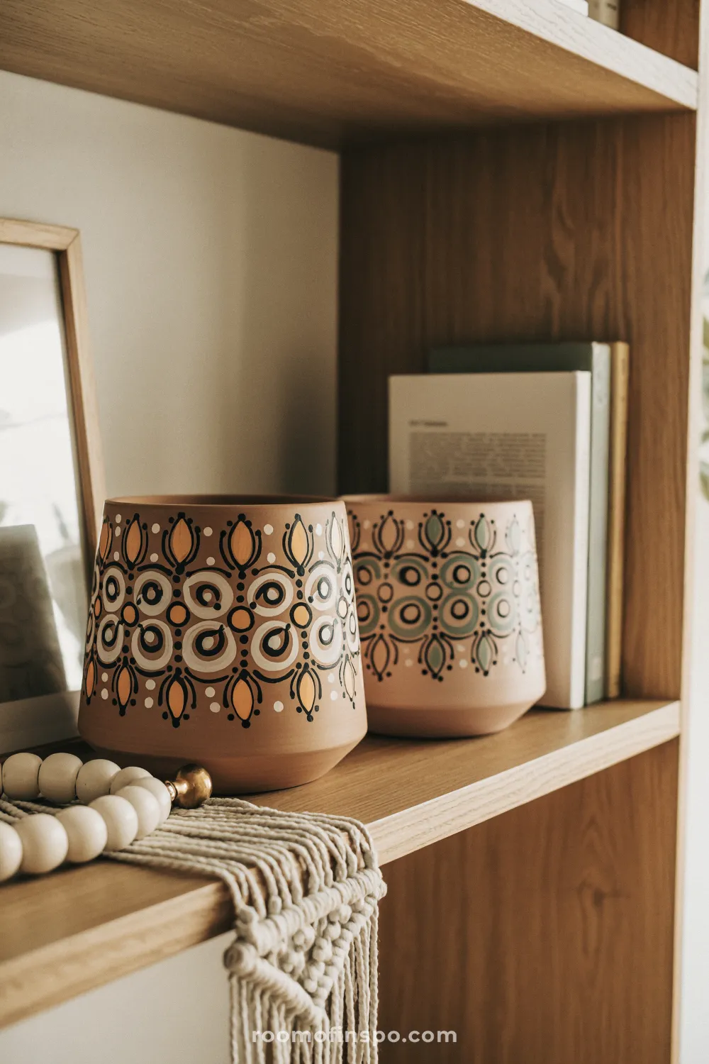Two mandala-painted terracotta pots on a boho shelf with neutral books and soft decorative accents.