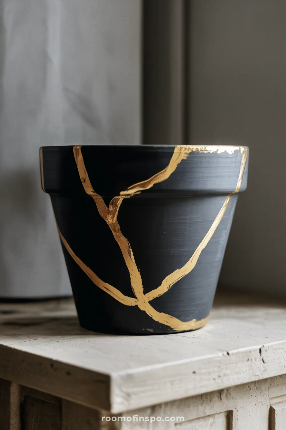 Matte black terracotta pot with hand-painted gold line accents on a pale stone surface.