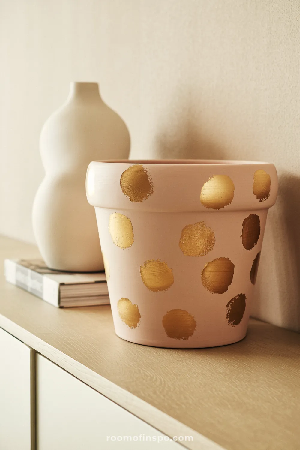 Blush terracotta pot with scattered gold dot accents styled on a light oak console table.